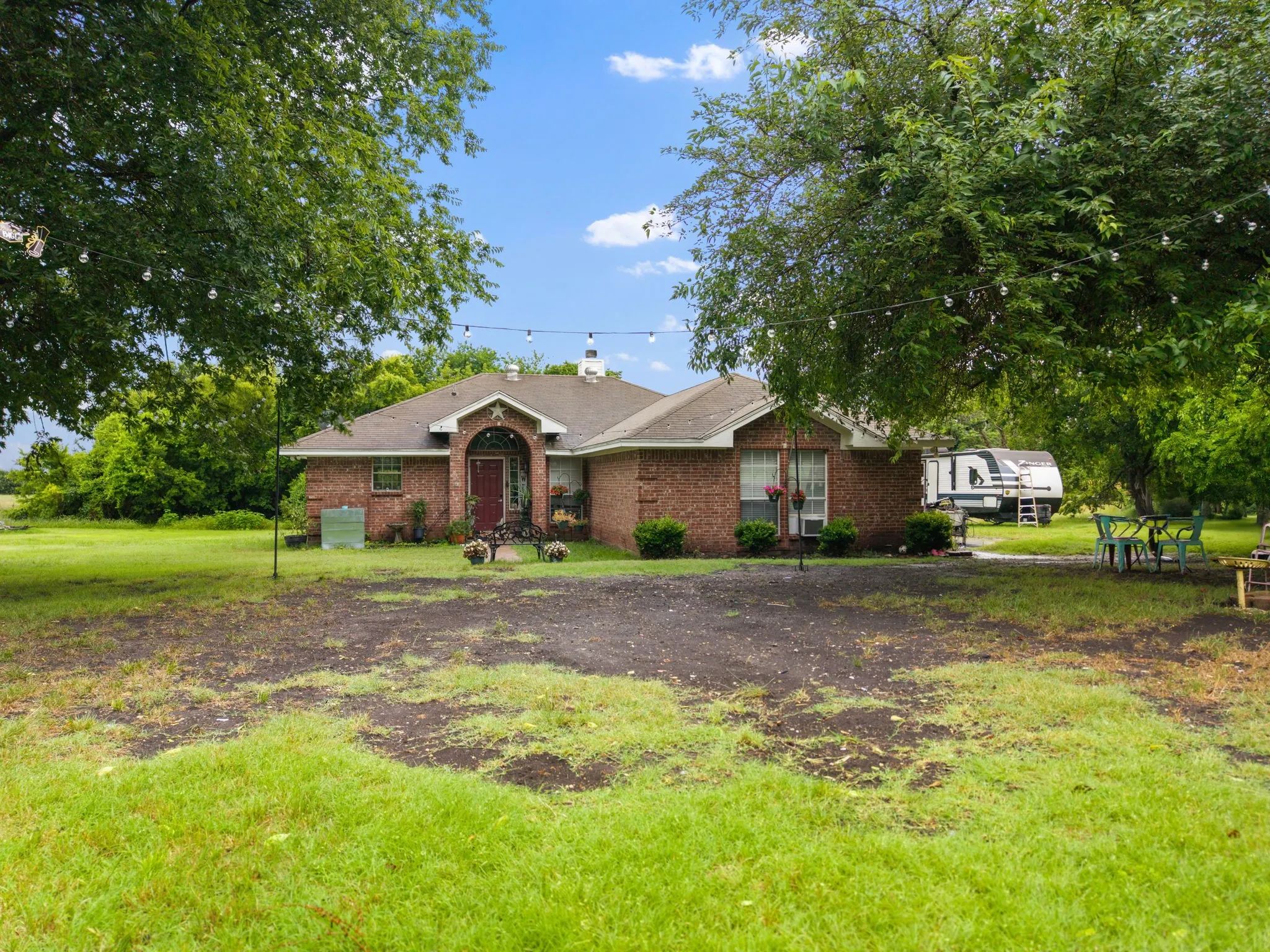 Brick exterior residence featuring a covered front entry, arched doorway, and mature trees