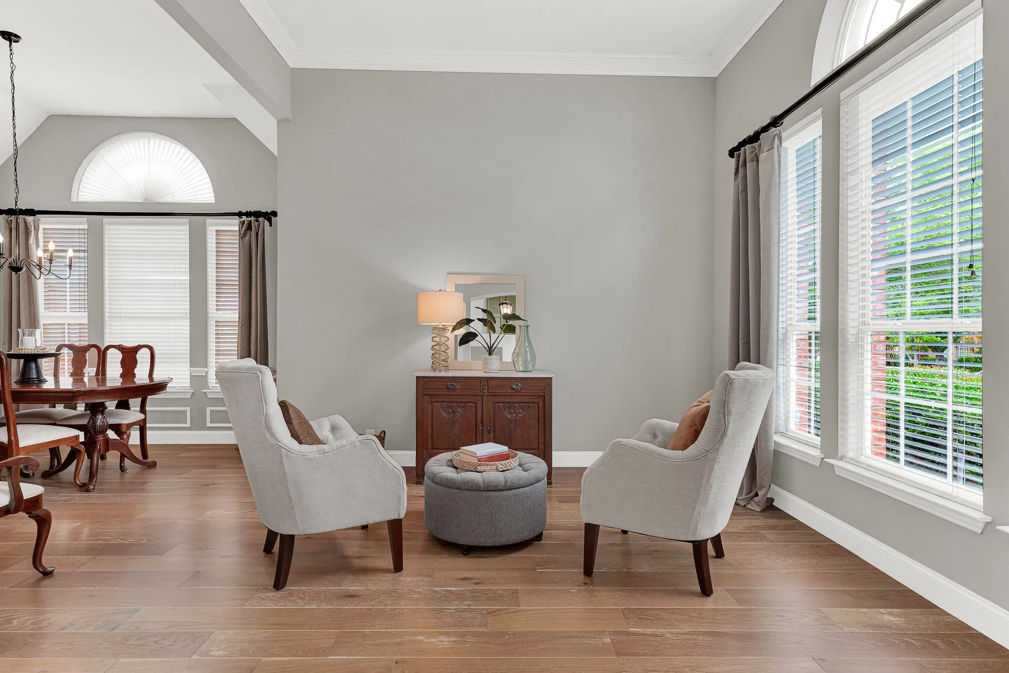 A graceful arched transom window crowns the corner wall while tall flanking windows pour afternoon light across wide-plank hardwood floors, making the space feel sun-drenched and airy. This is the quiet room at the front of the house where a slow Sunday morning actually feels slow.