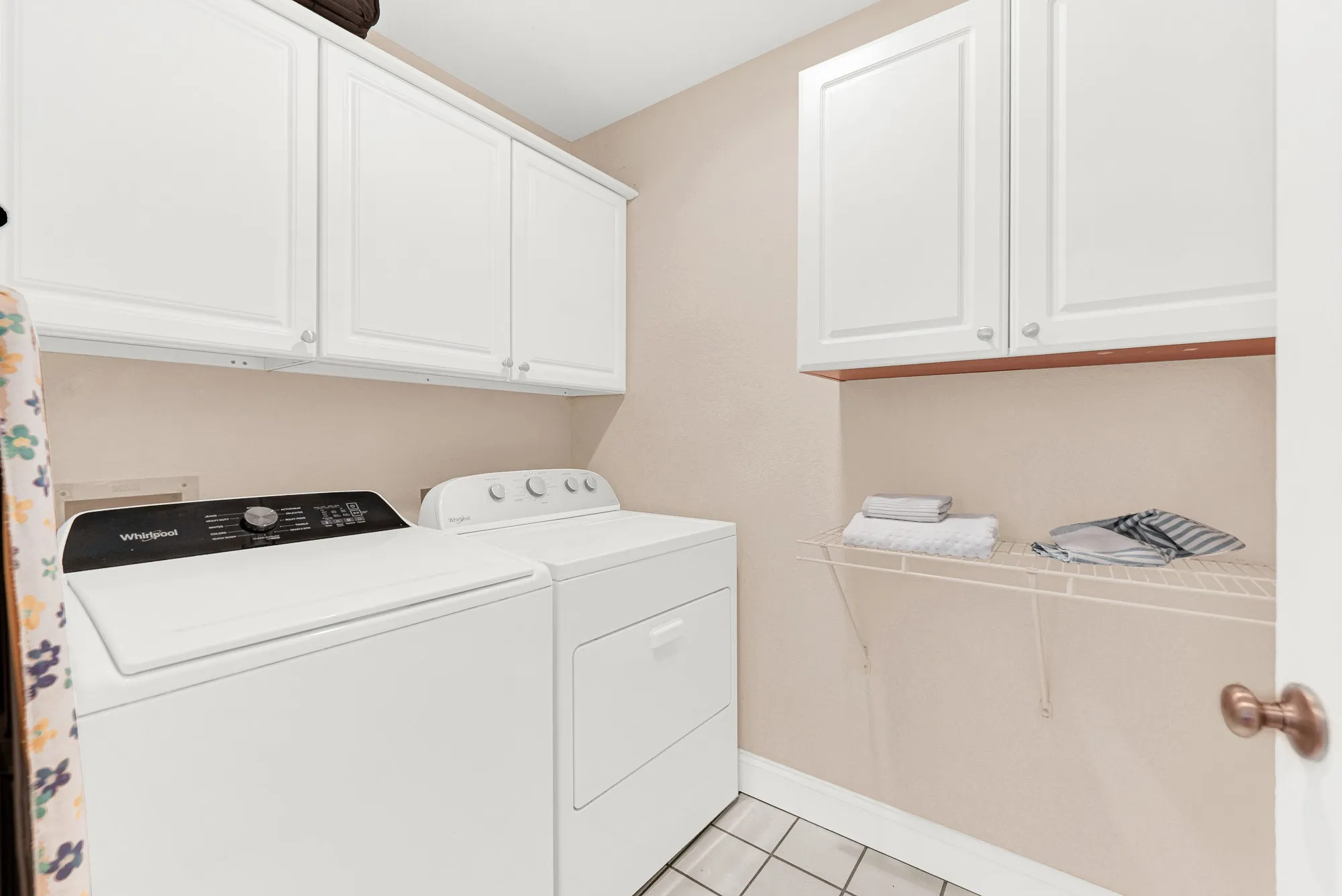 Crisp white cabinetry lines the upper walls, maximizing the efficiency of this brightly illuminated service space. You can easily transition from the garage after a busy day, dropping off items right onto the durable tiled flooring.
