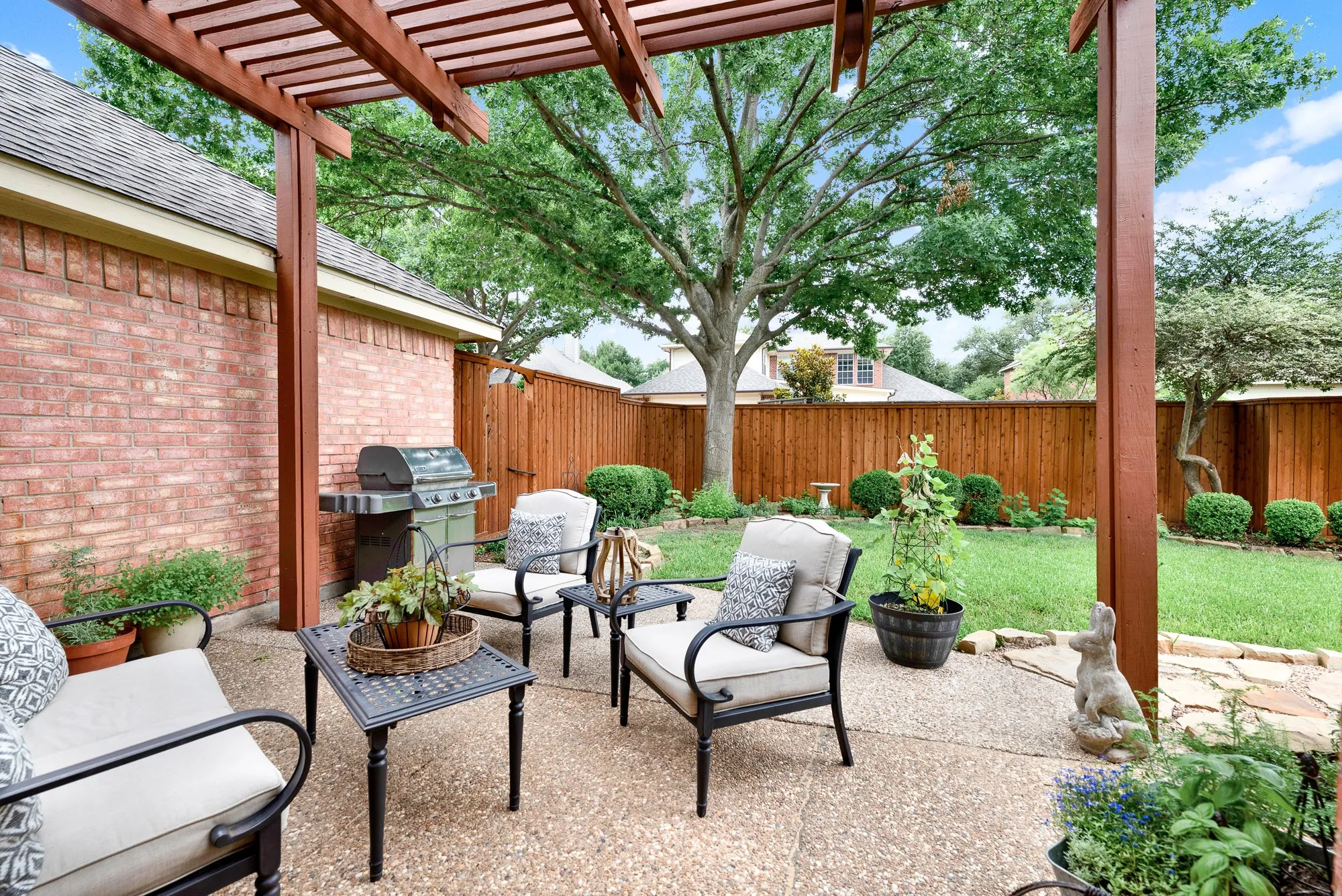 A substantial wooden pergola filters the afternoon sun, casting geometric shadows across the textured aggregate patio. Enjoy a quiet weekend afternoon listening to the rustle of leaves from the mature shade tree just beyond the patio edge.
