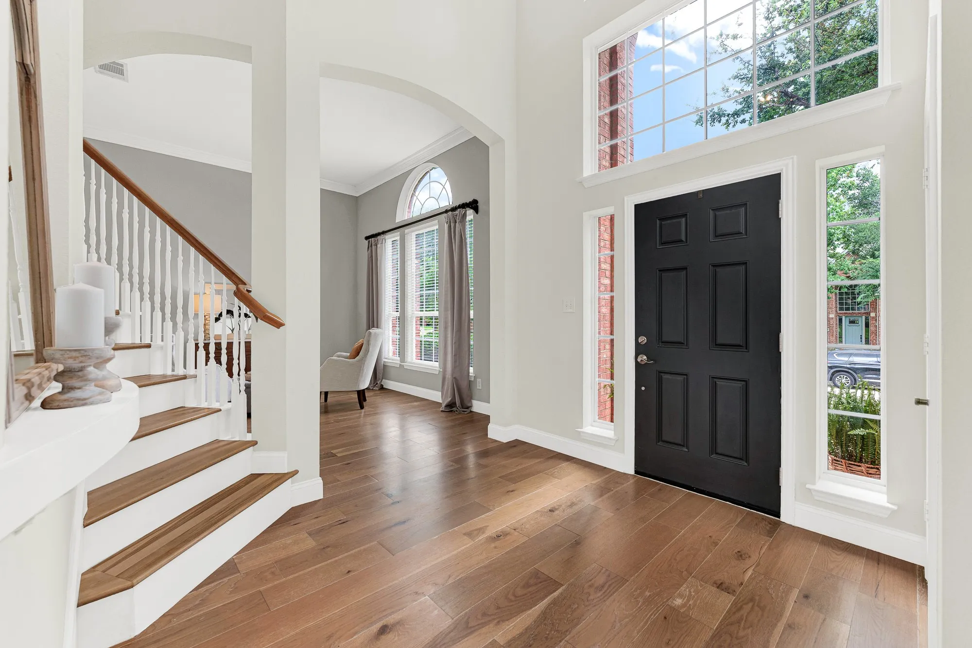 A soaring two-story window wall beside the black front door floods the entry with natural light, while wide-plank hardwood floors and a sweeping staircase set an immediately warm and welcoming tone. Every single person who walks through that door stops for just a moment — this entry earns it