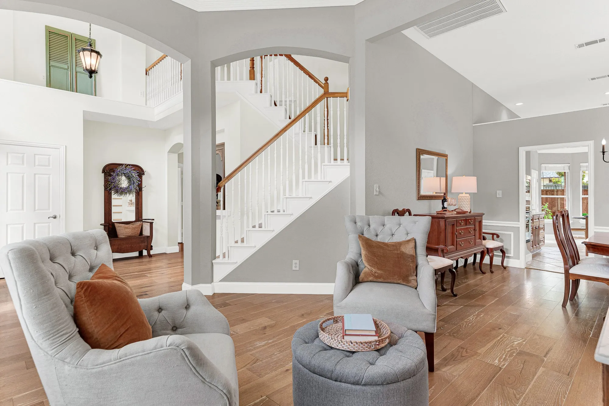Soaring ceilings with crisp crown molding draw the eye upward toward the open staircase landing above, while arched passageways on either side keep the whole first floor feeling connected and effortlessly open. Guests naturally drift through here, never quite sure where the living room ends and the rest of the home begins