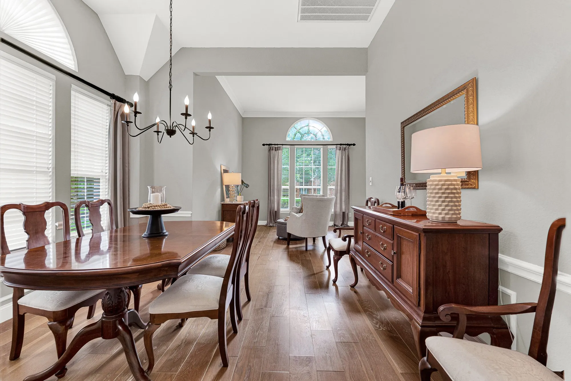The vaulted ceiling peaks at the far end where an arched window frames a green view, creating a natural focal point that makes the long, gracious room feel both grand and intimate. Afternoon light moves slowly across these hardwood floors all day long — it's the kind of thing you notice and love.