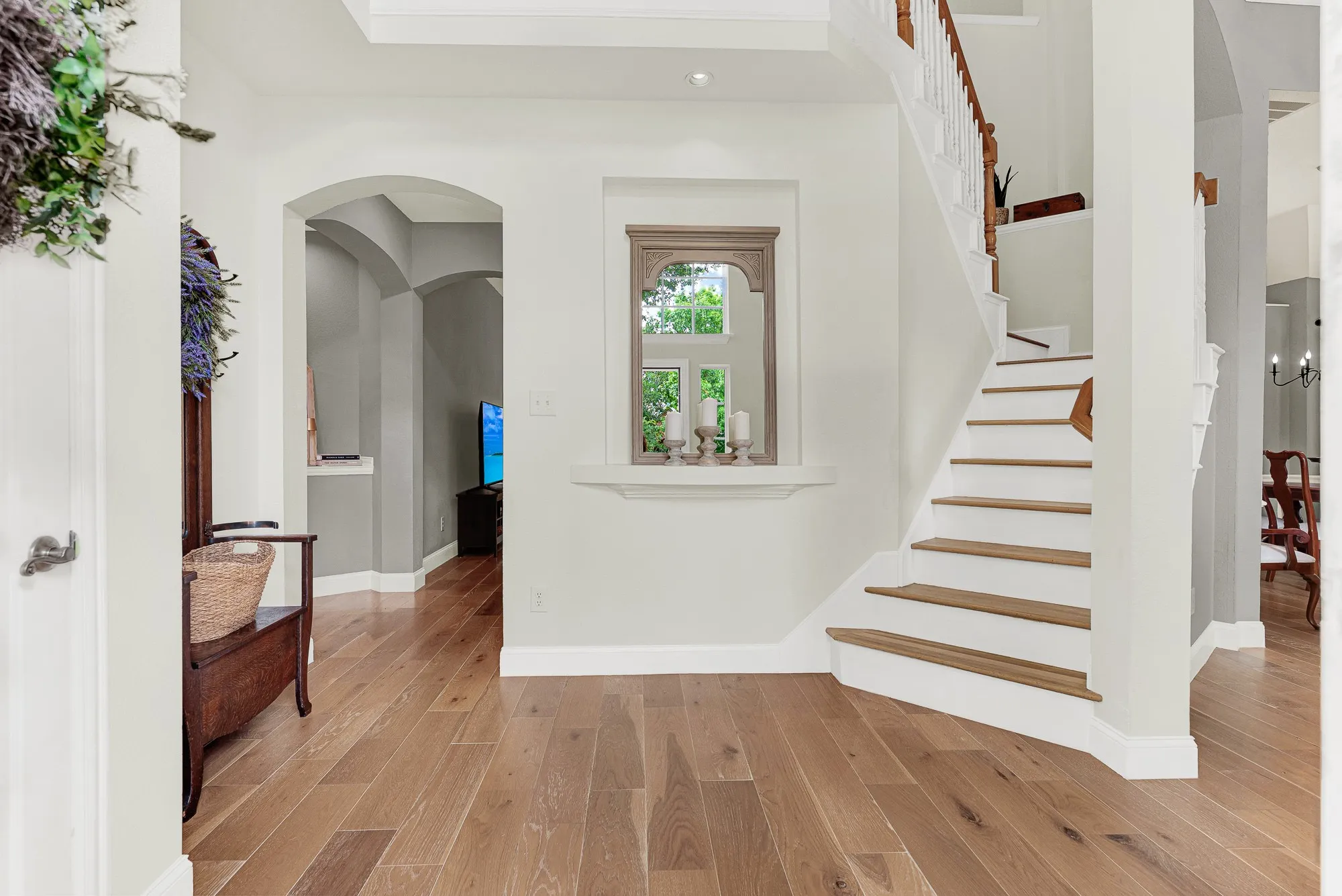 A charming built-in display niche with decorative molding is framed by the graceful curve of the staircase on one side and an arched passageway on the other, creating a foyer that feels both intimate and architecturally layered. Coming home feels different when the entry itself is this considered and calm.
