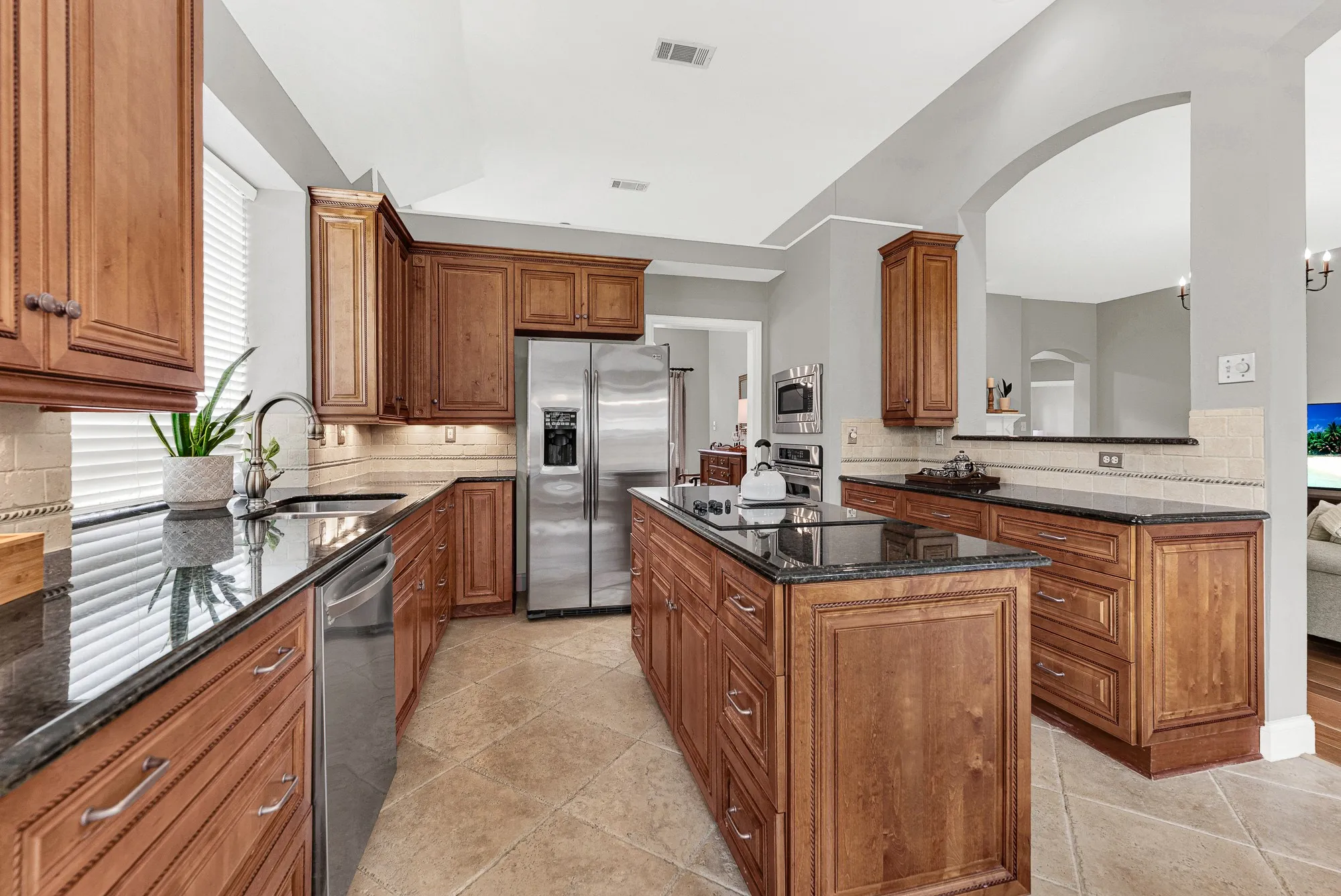 The kitchen opens through a graceful arch into the family room beyond, keeping the cook connected to the rest of the home while the vaulted ceiling above adds unexpected volume. Weeknight dinners feel easy here — the layout was made for people who actually cook.