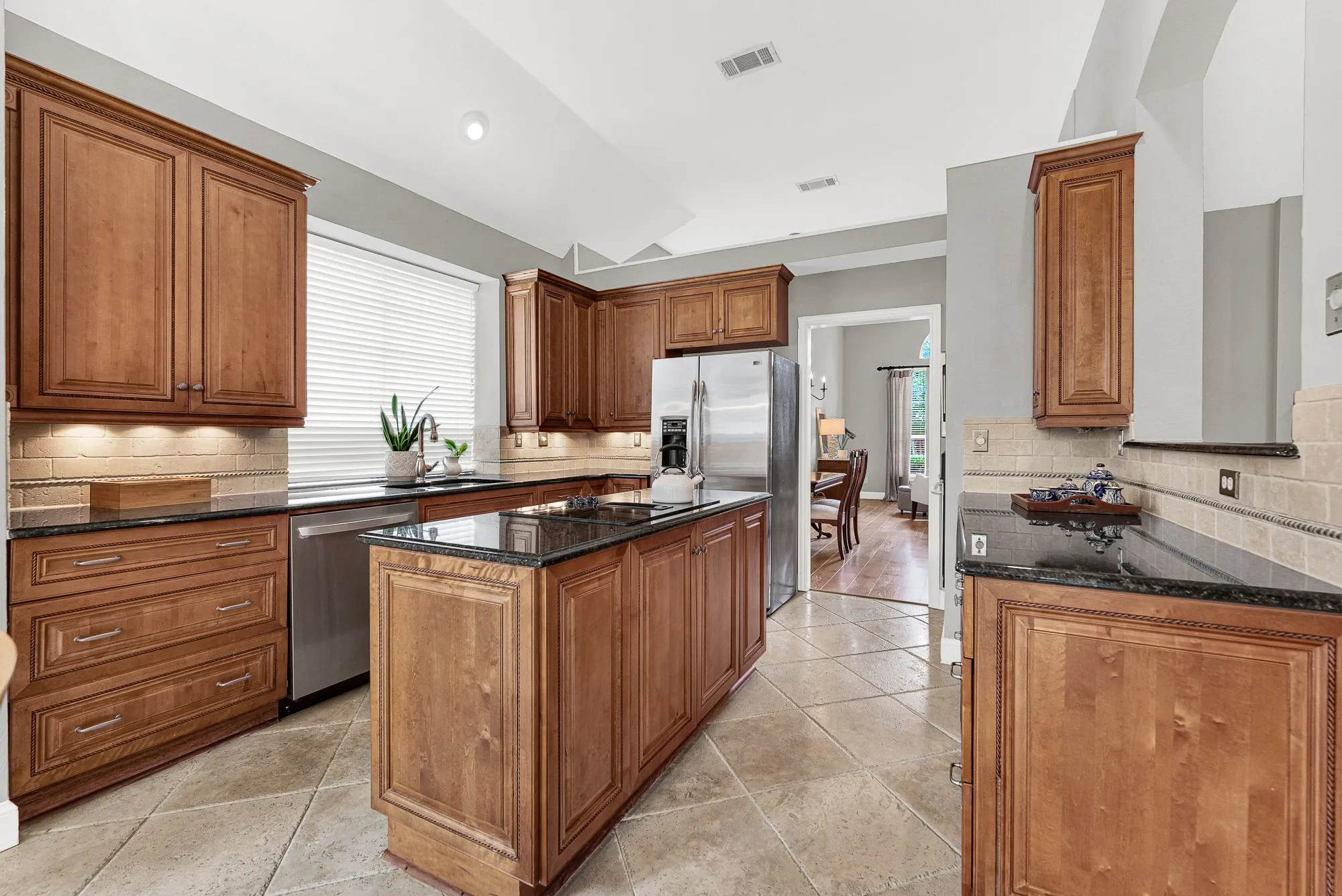 Under-cabinet lighting glows warmly across the rope-detailed custom cabinetry and travertine backsplash, while large-format tile floors anchor the space with quiet elegance. This is a kitchen that rewards the cook — every inch of counter and cabinet space was thought through carefully.