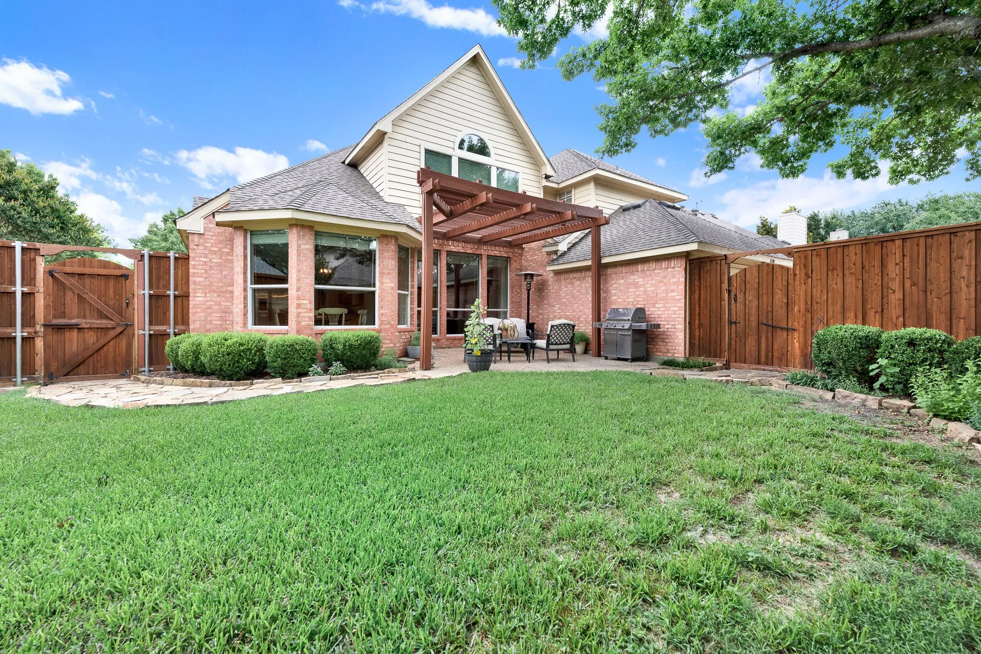 The classic brick elevation peaks with a wall of large windows and an arched accent window that mirrors the open blue sky. Picture hosting a lively summer barbecue where guests easily mingle between the open-air patio and the indoor kitchen.