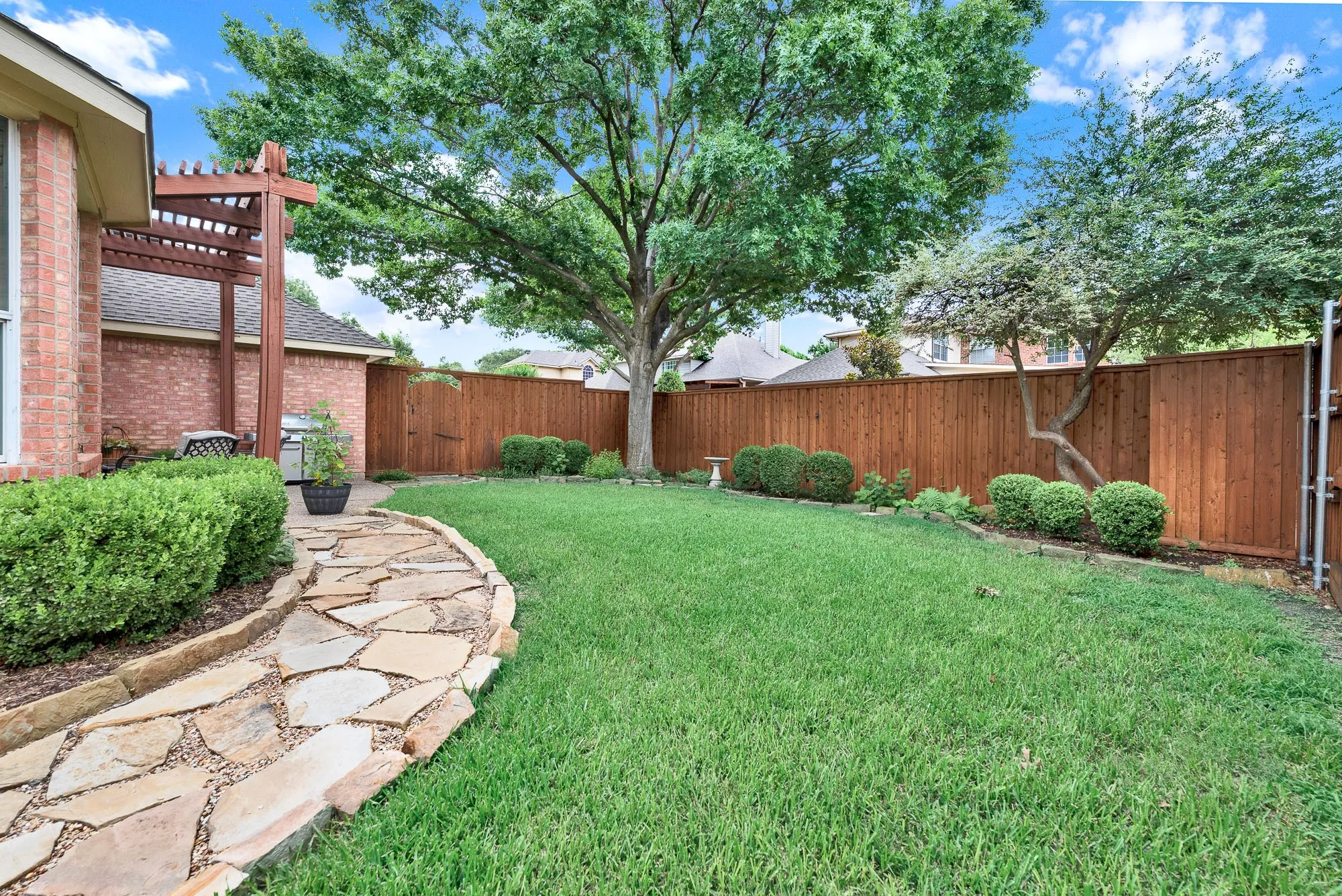 A winding flagstone path curves gracefully along the lawn, leading the eye beneath the canopy of a sprawling shade tree. Take a peaceful morning stroll with your coffee, appreciating the crisp air and the neatly manicured perimeter landscaping.