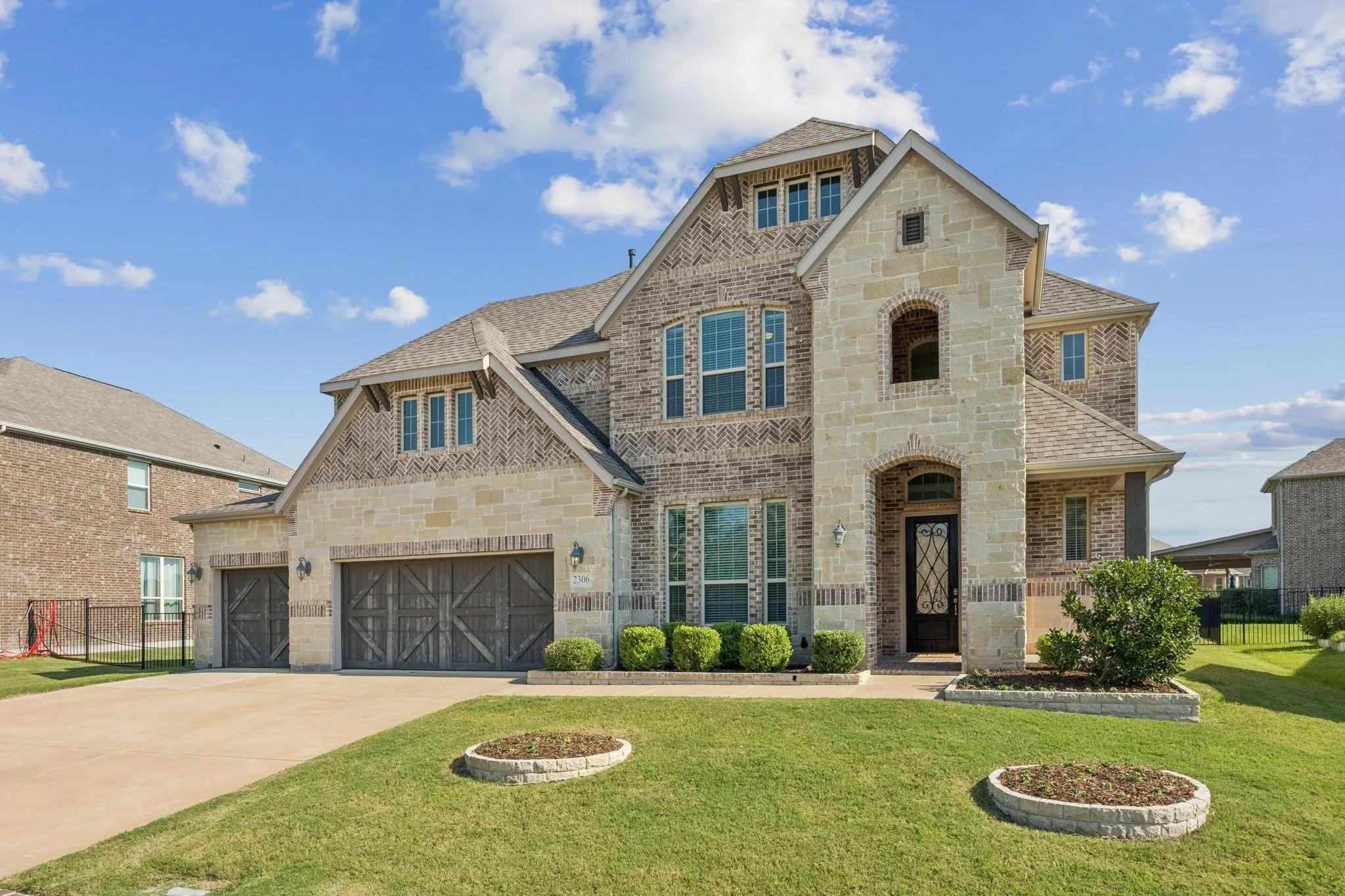 Stone and brick facade featuring a covered entry, decorative garage doors, multiple gables, and a landscaped front yard with planting beds