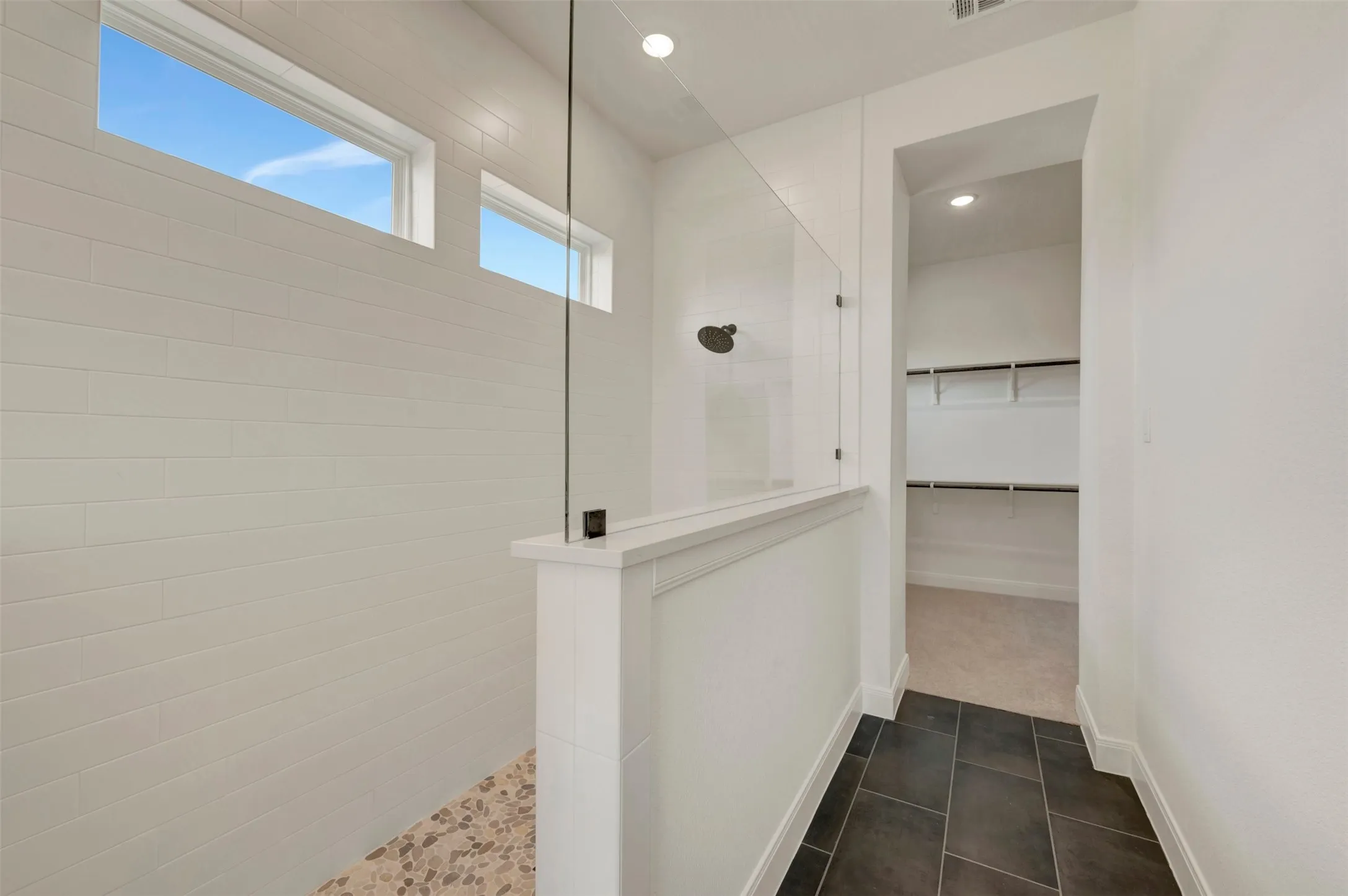 Walk-in shower with clear glass enclosure, white subway tile walls, and pebble-finish floor