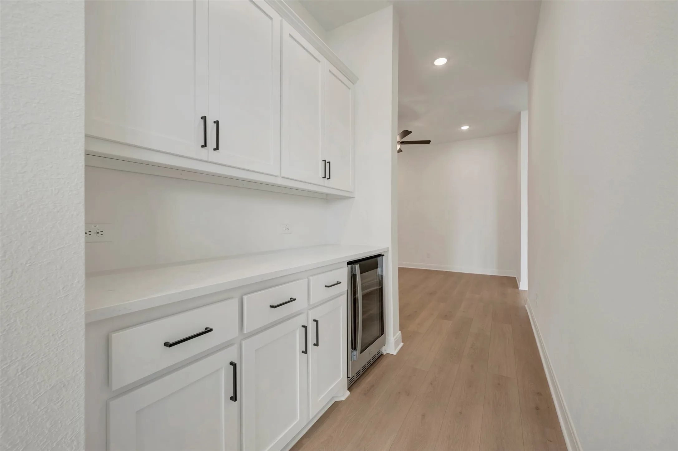 Built-in cabinetry with matte black hardware, integrated beverage cooler, wood-finish flooring, and recessed lighting