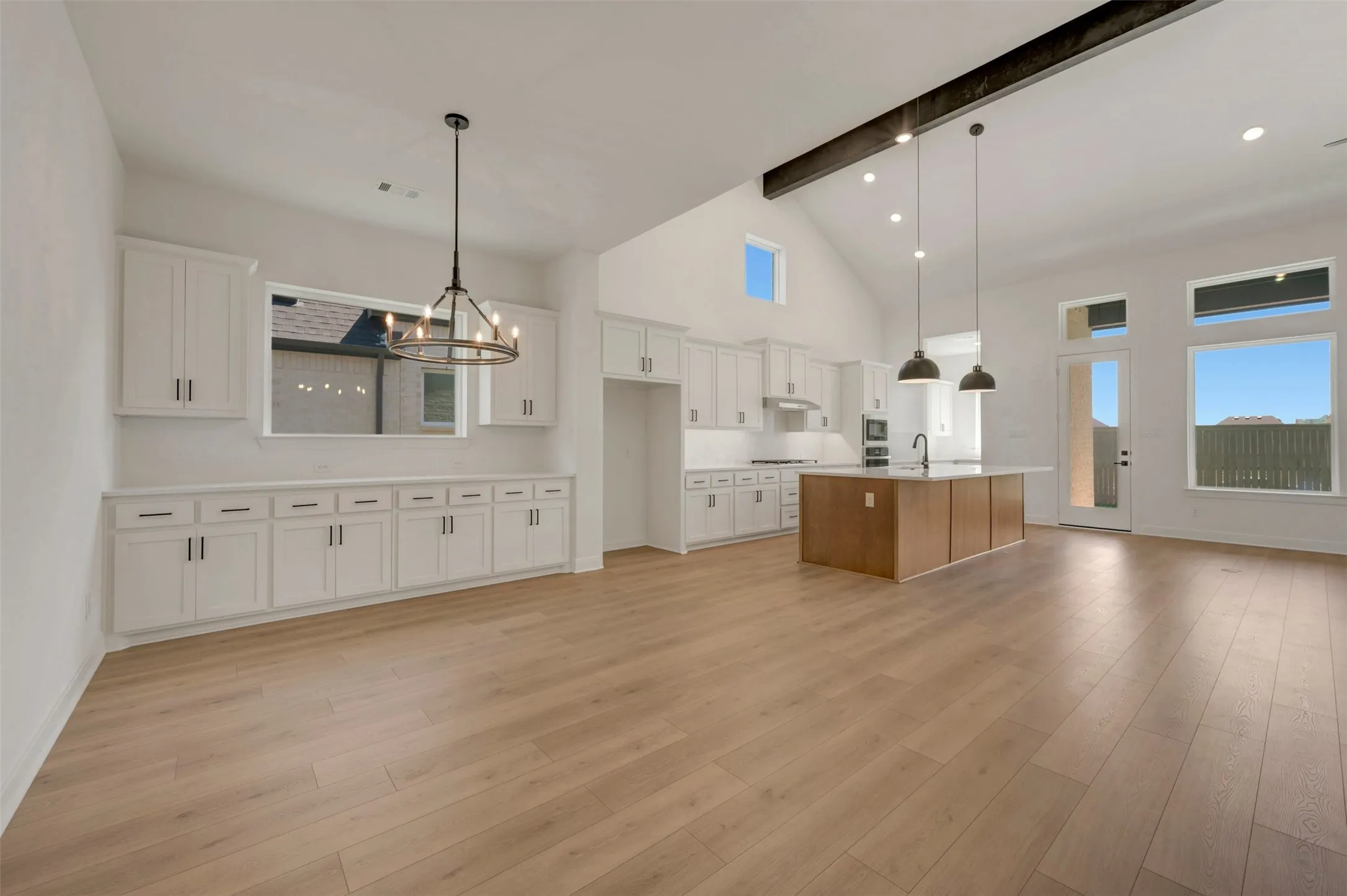 Vaulted ceiling with an exposed beam, wood-finish flooring, white cabinetry, a kitchen island with seating, and a glass-paneled exterior door