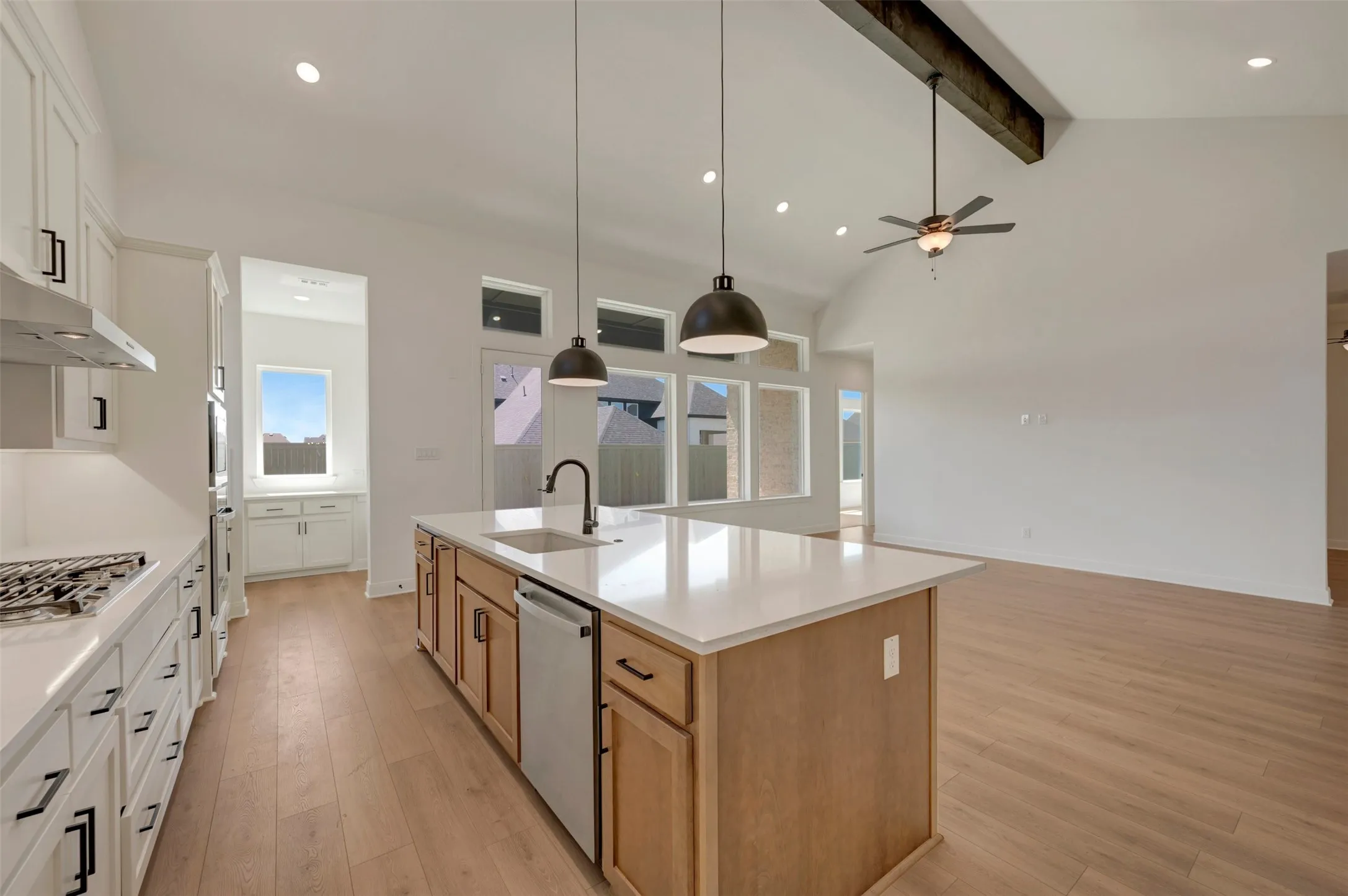Gourmet kitchen with a large island, white perimeter cabinetry, stainless steel appliances, and wood-finish flooring, complemented by a vaulted ceiling