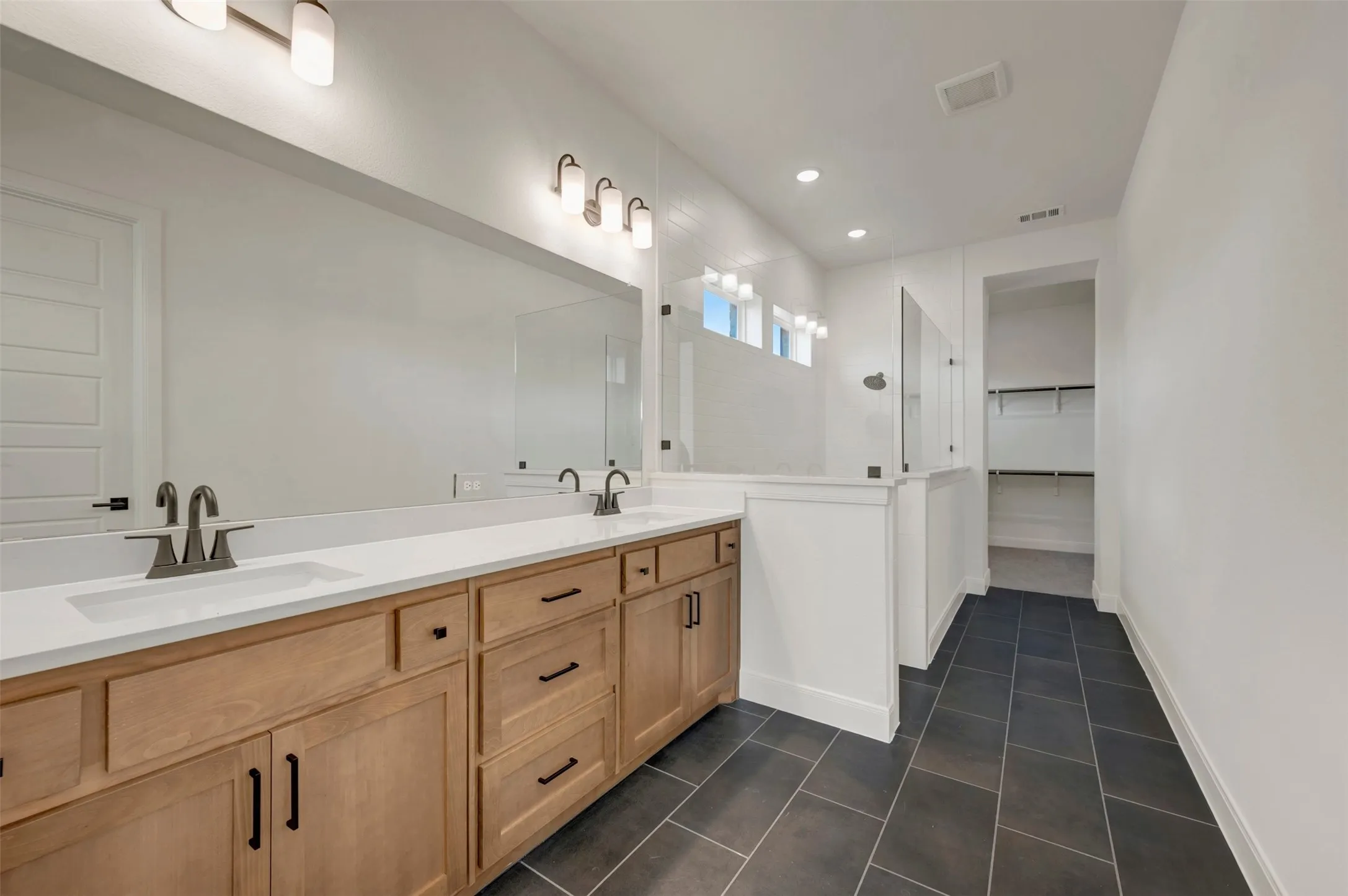Dual sink vanity with light wood finish cabinetry, white countertops, and dark hardware