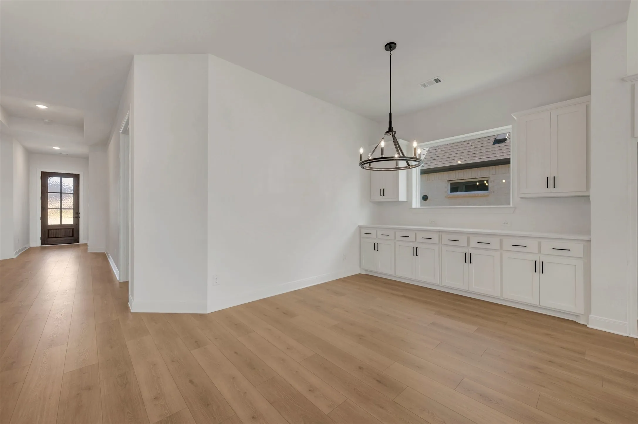 Wood-finish flooring throughout, white cabinetry with dark hardware, built-in storage, and a suspended black chandelier