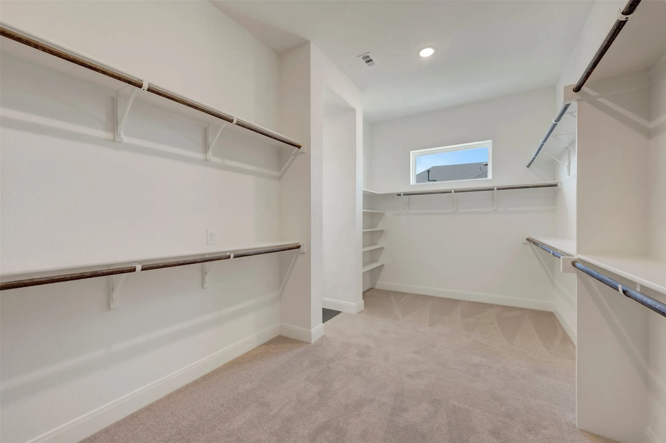 Expansive walk-in closet featuring built-in shelving, hanging rods, carpet flooring, and a recessed ceiling light fixture