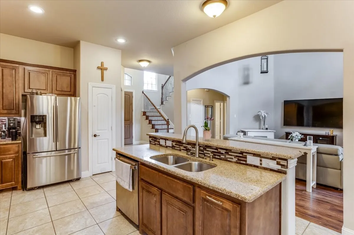 Kitchen with stainless steel refrigerator, warm wood cabinetry, and a double basin sink