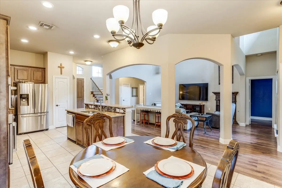 Open-concept dining area with tile flooring and a traditional chandelier, opening to a kitchen featuring wood cabinetry and stainless steel appliances