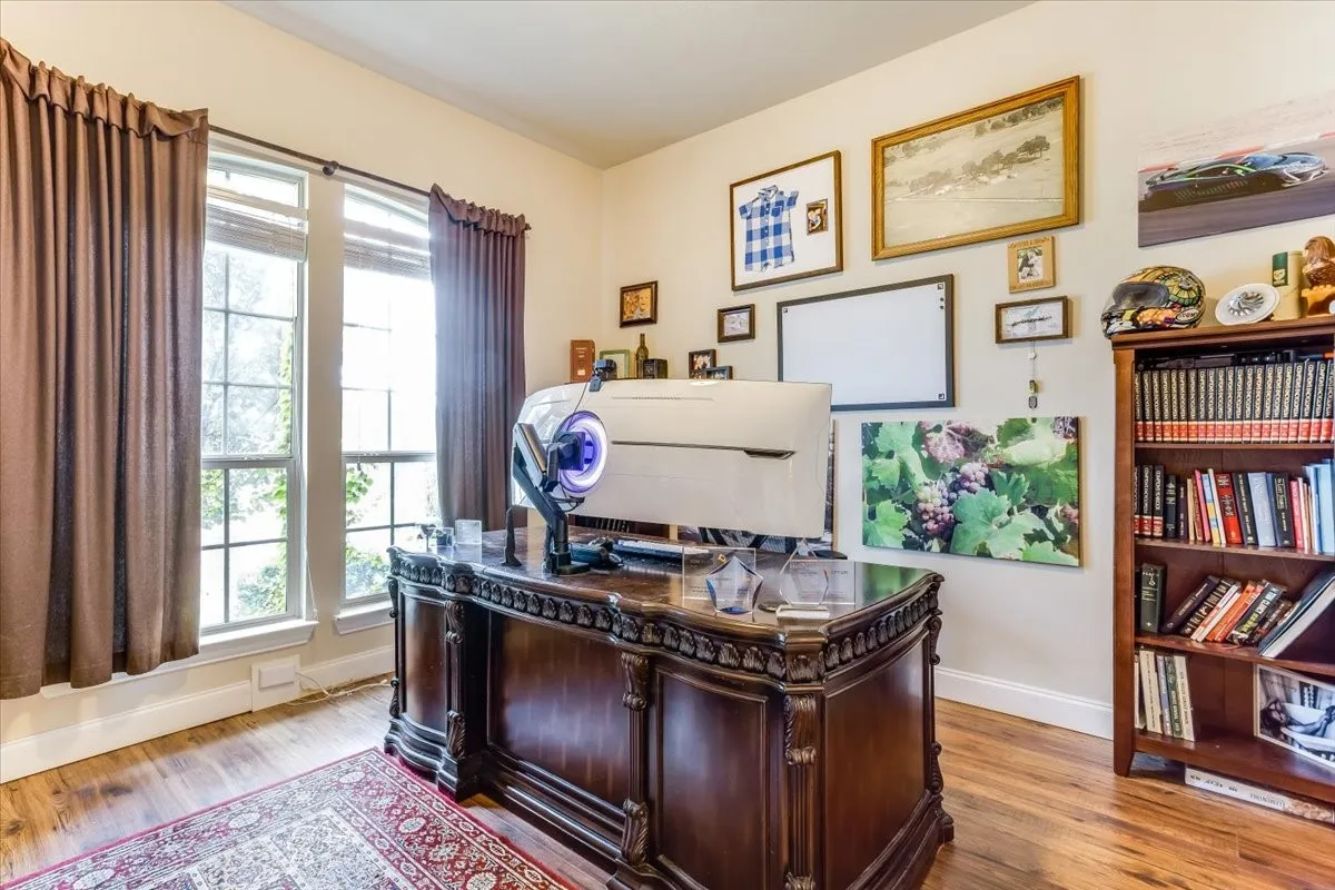 Room featuring wood-finish flooring, two window openings with exterior views, and a prominent dark wood built-in bookcase