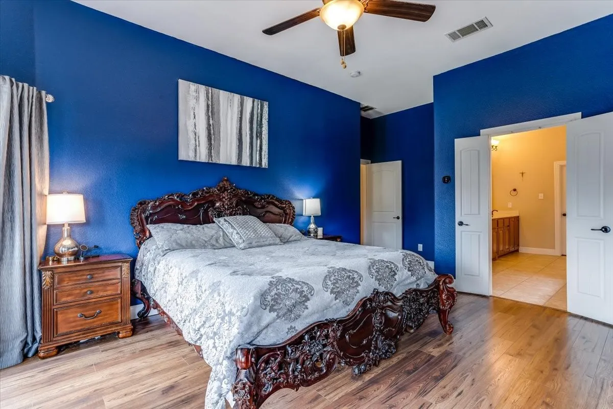 Spacious sleeping area featuring wood-finish flooring, a ceiling fan, and double doors opening to a separate space with a vanity