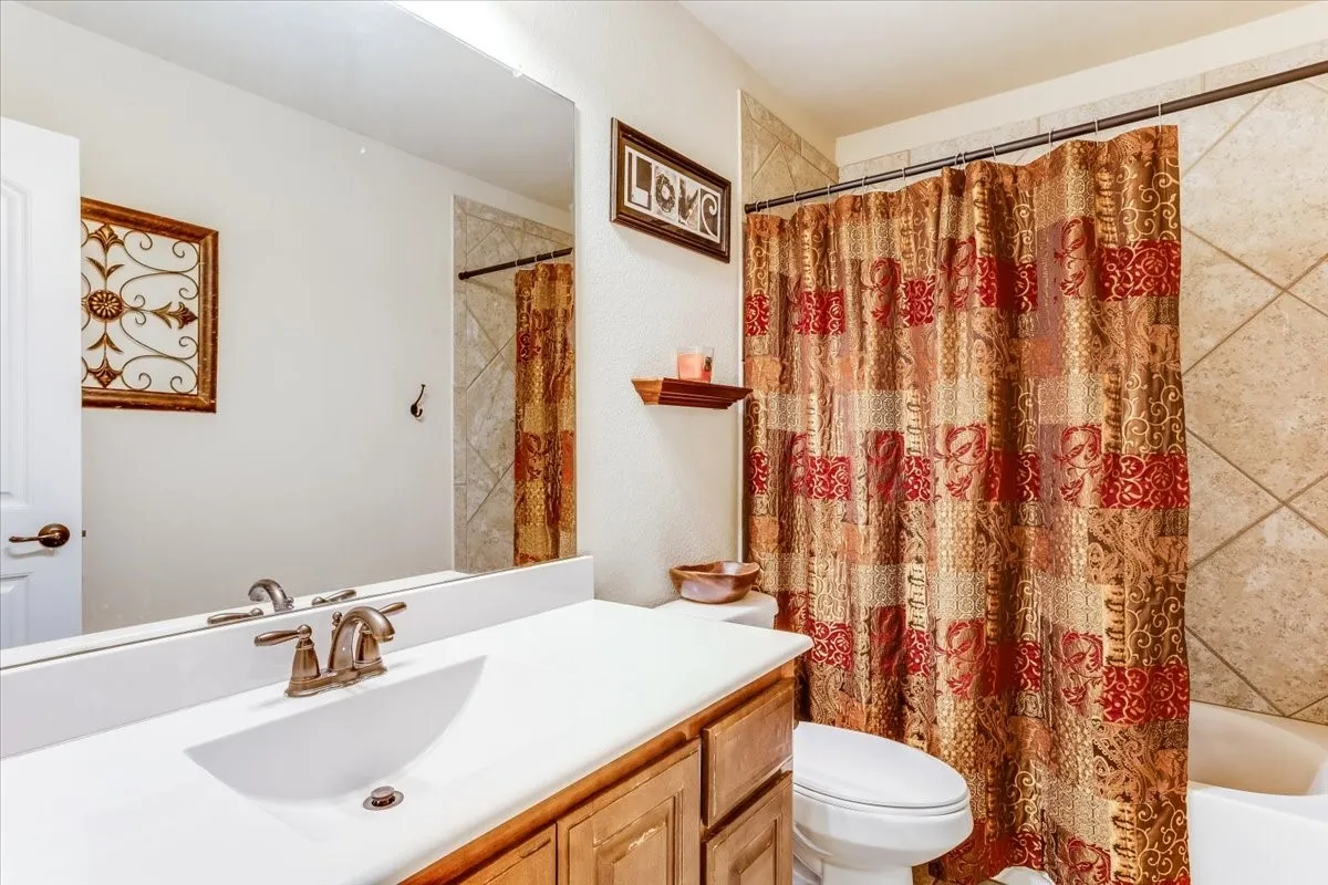 Bathroom featuring a wood-finish vanity with a white countertop and integrated sink, a large wall-mounted mirror, and a ceramic tile shower surround