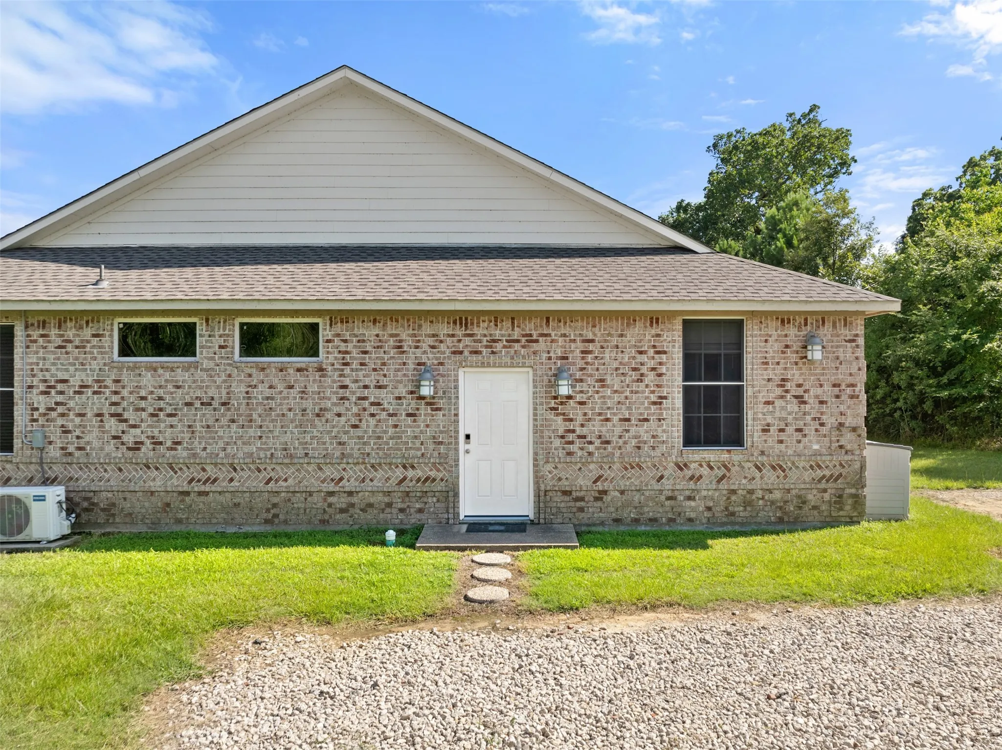 Brick exterior featuring a white entry door, exterior sconce lighting, and a pitched roofline