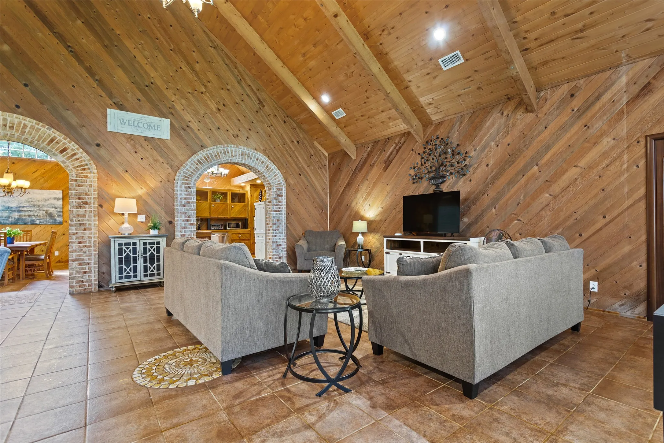 Vaulted wood-paneled ceilings with exposed beams, wood-plank walls, and terracotta-toned tile flooring with an inlaid mosaic detail