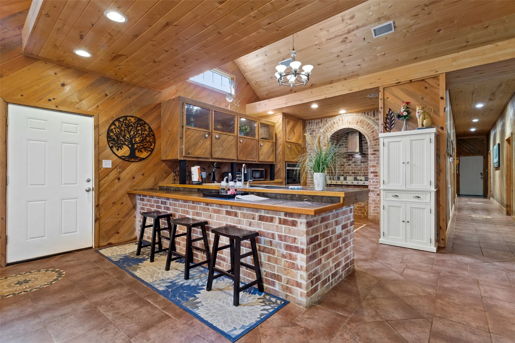 Open-concept kitchen featuring a brick-faced island with seating, wood-finish cabinetry, and recessed lighting