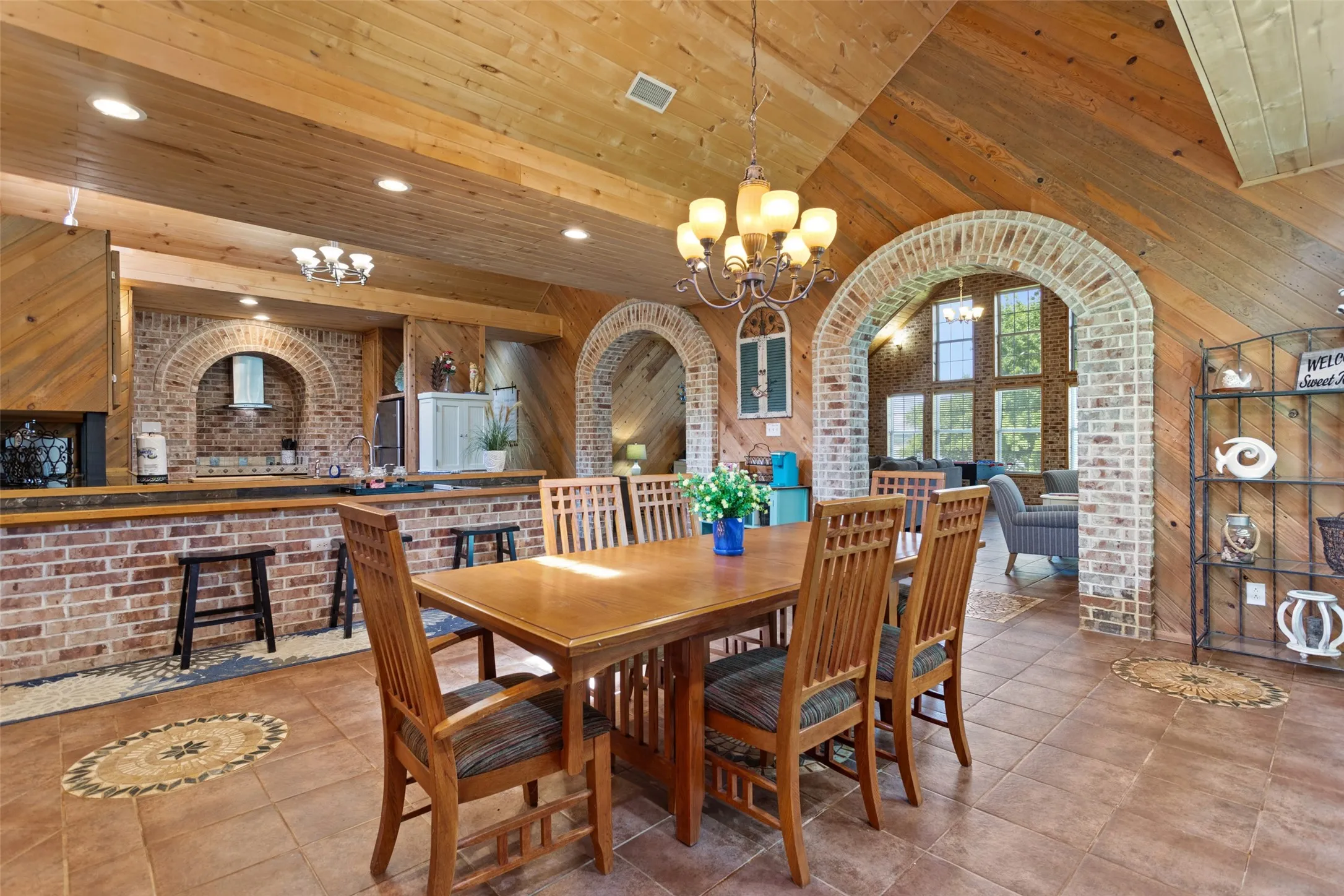 Spacious dining area featuring a vaulted wood-paneled ceiling, ceramic tile flooring with decorative inlays, and brick archways