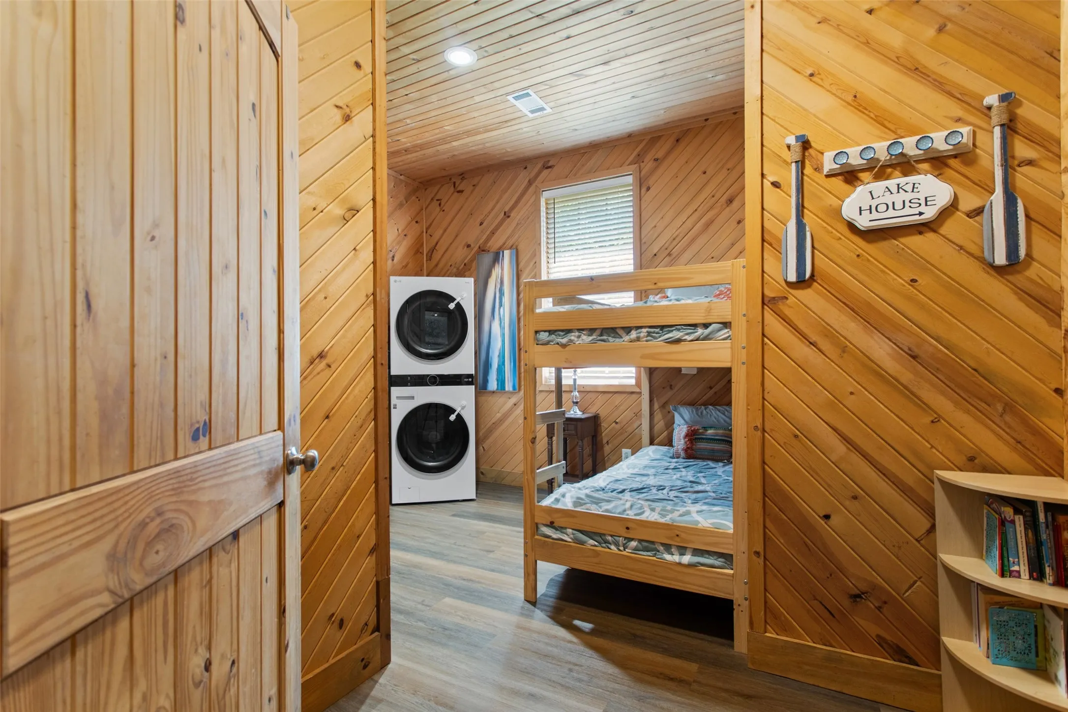 Room featuring wood-planked walls and ceiling, a bunk bed, and a stacked washer and dryer unit