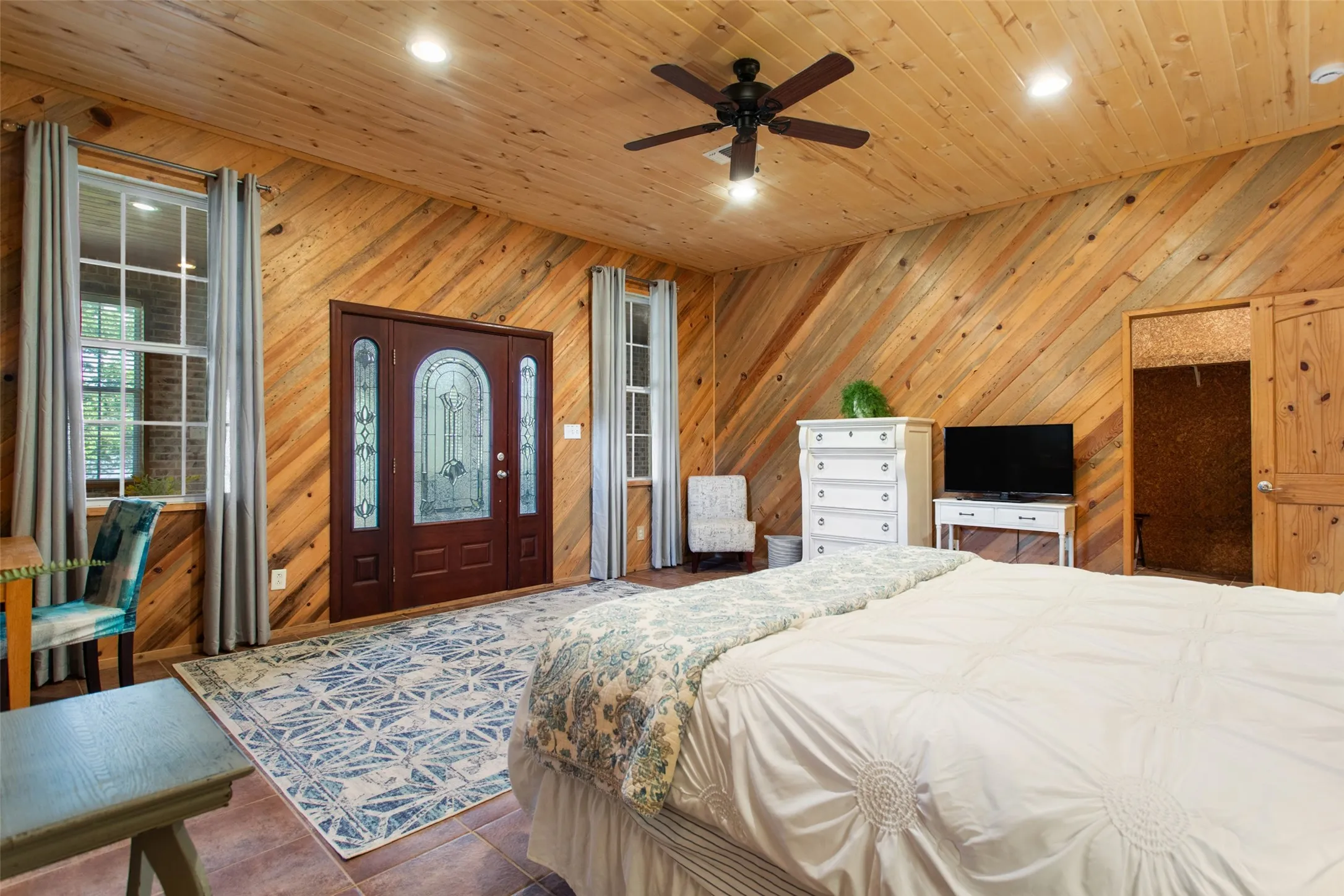 Wood-paneled room featuring a decorative front entry door with sidelights, two double-hung windows, and a ceiling fan with integrated lighting