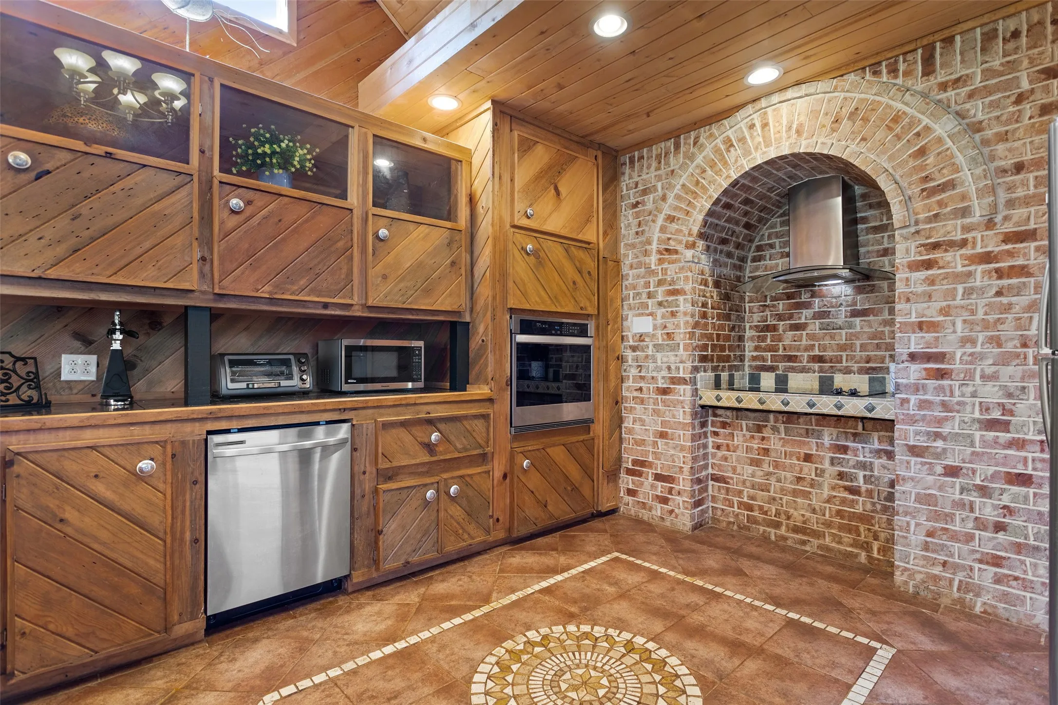 Kitchen featuring custom wood cabinetry with glass-front accents, stainless steel dishwasher, and built-in wall oven