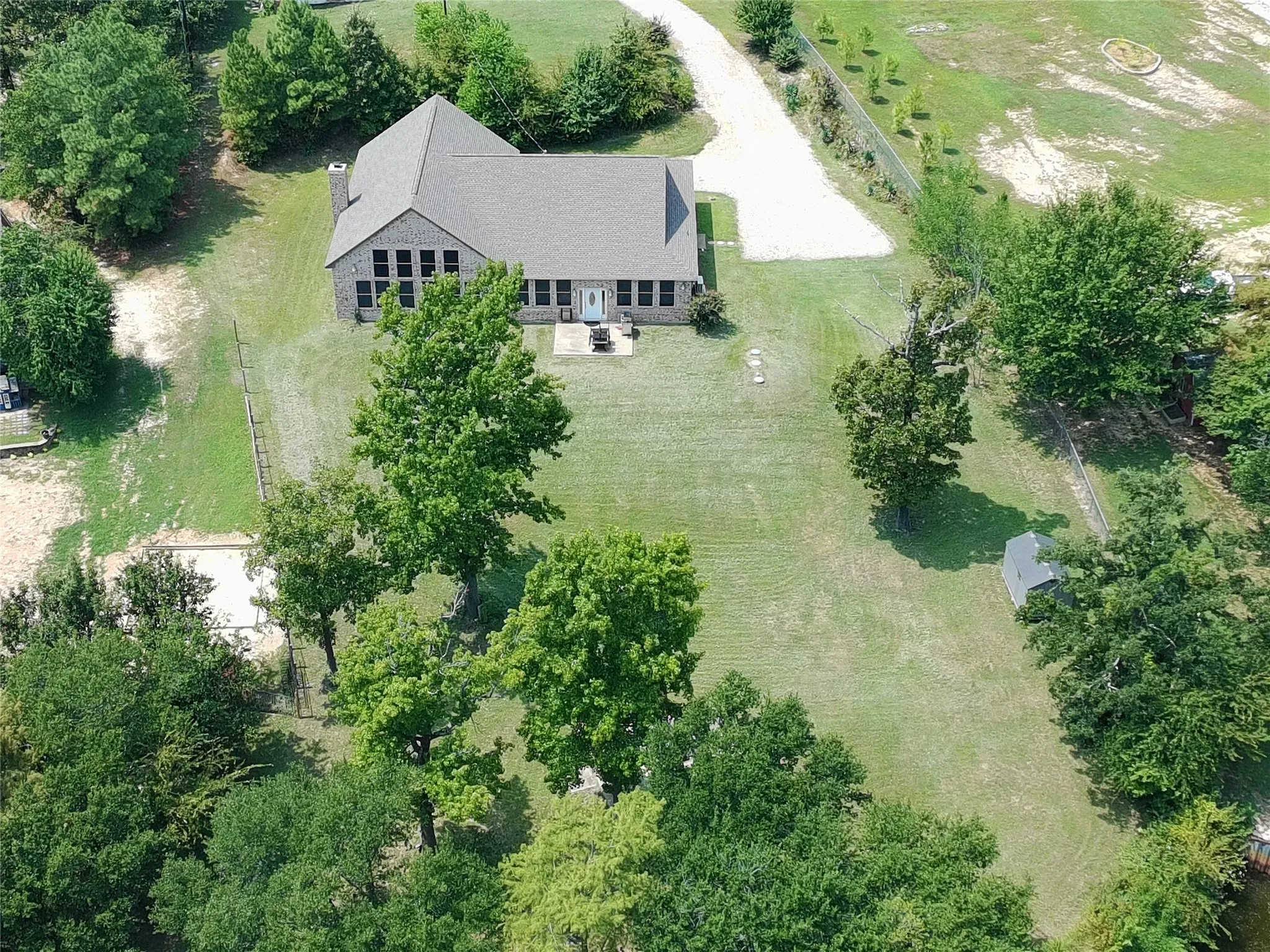 Expansive property featuring a brick exterior residence with mature trees, and a long driveway
