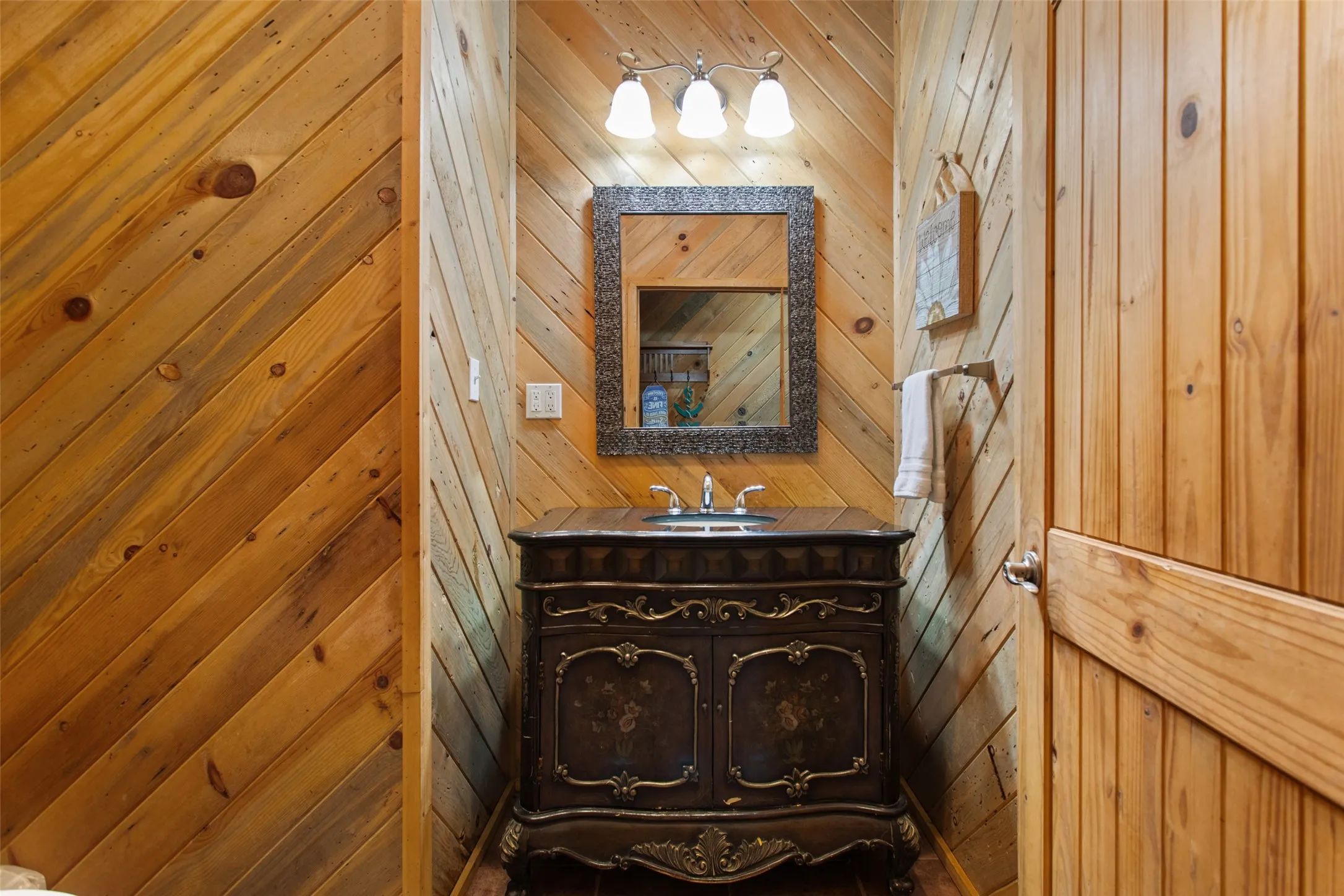 Wood-paneled room featuring a decorative vanity with an integrated sink, polished chrome faucet, and a wall-mounted mirror