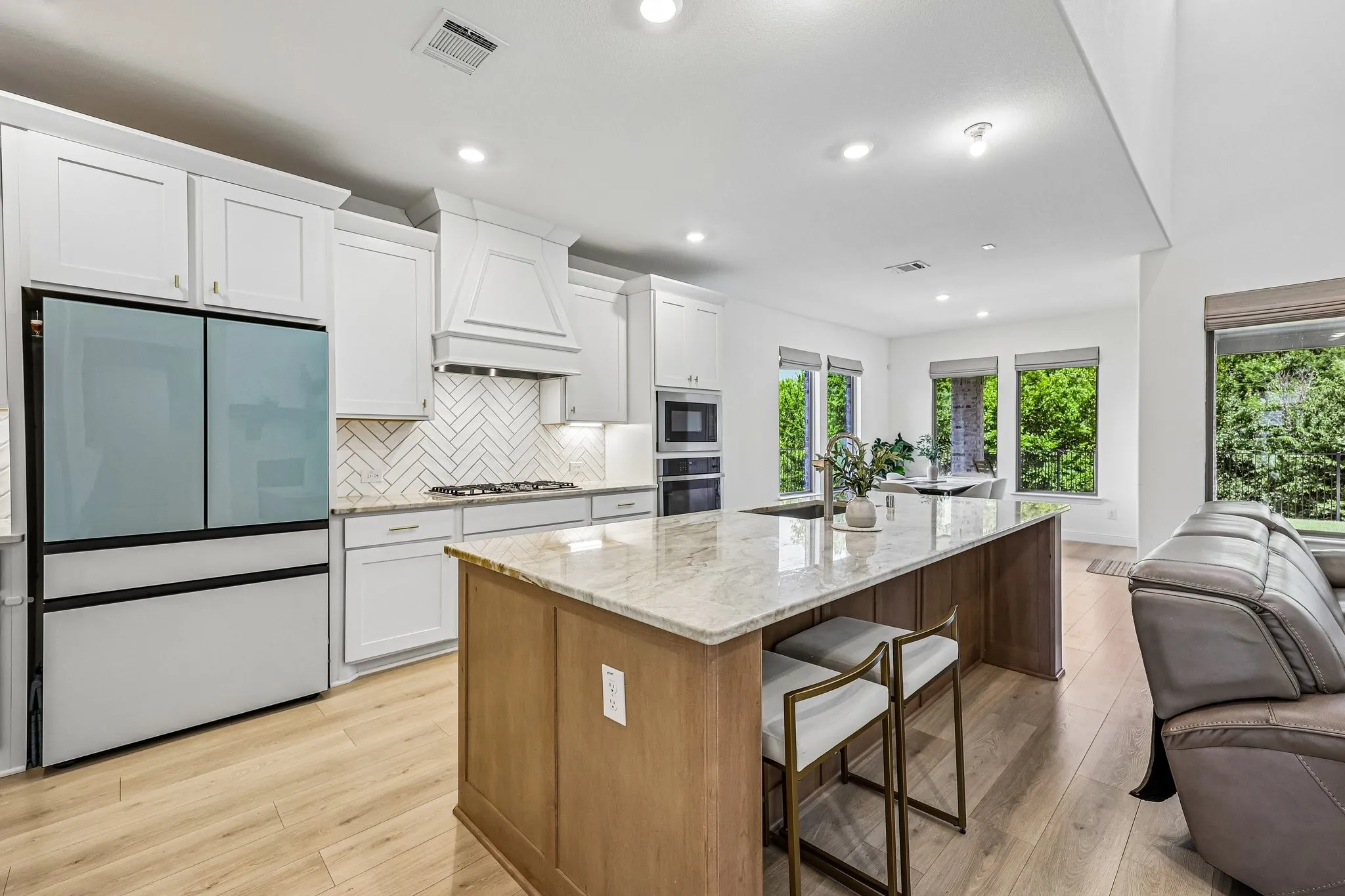 Open-concept kitchen featuring an oversized island with countertop seating, white shaker cabinetry, a herringbone tile backsplash, and wood-finish flooring