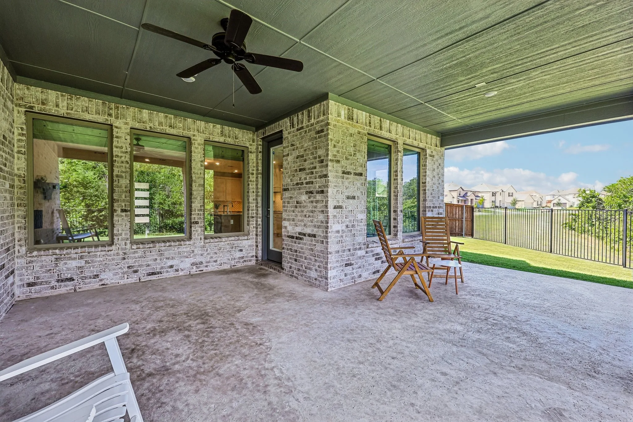 Covered patio featuring a ceiling fan, light gray brick exterior, concrete flooring, and a black wrought iron fence