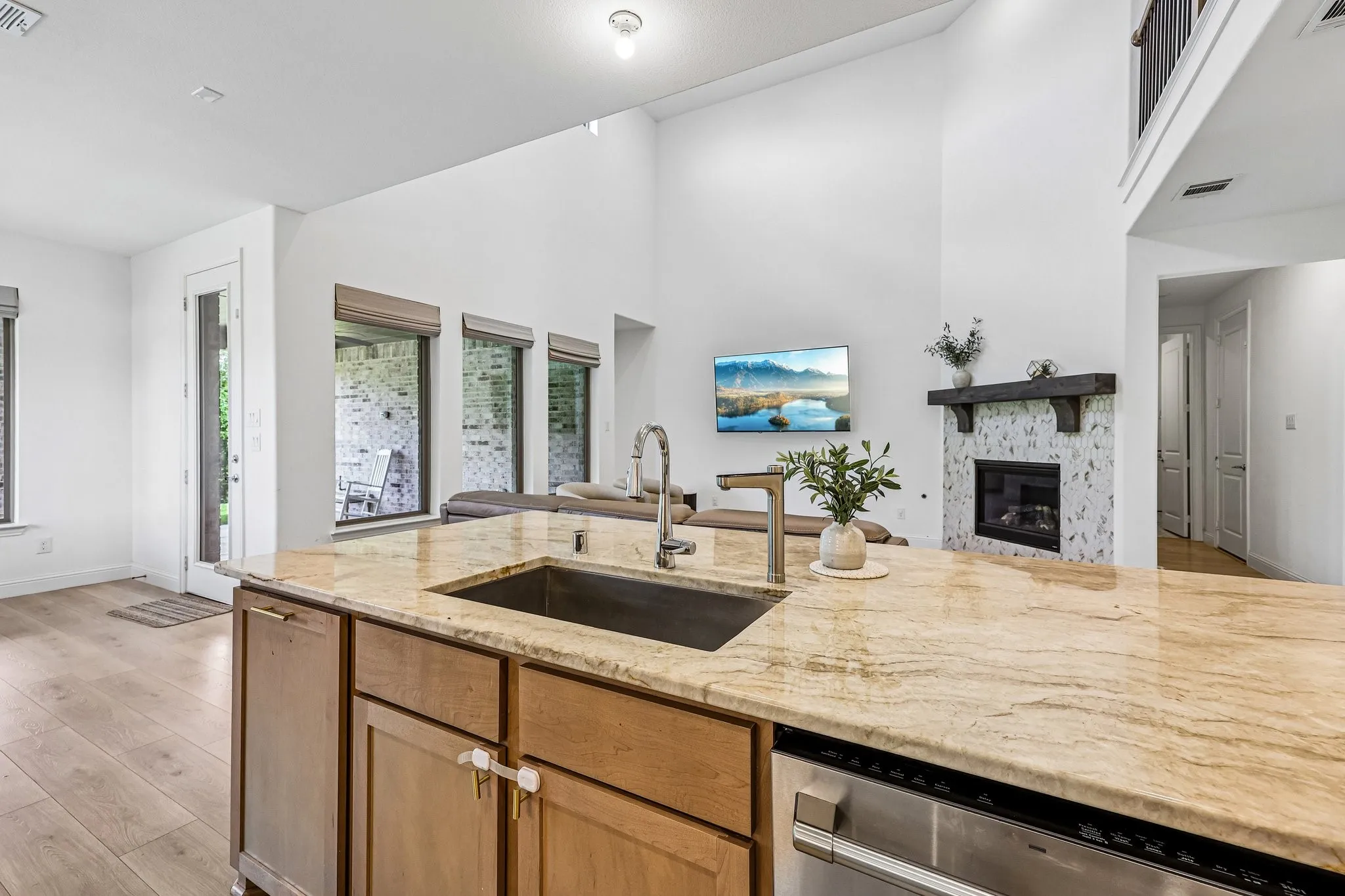 Kitchen island featuring a single-basin sink with a gooseneck faucet, light-toned granite countertop, and integrated stainless steel dishwasher