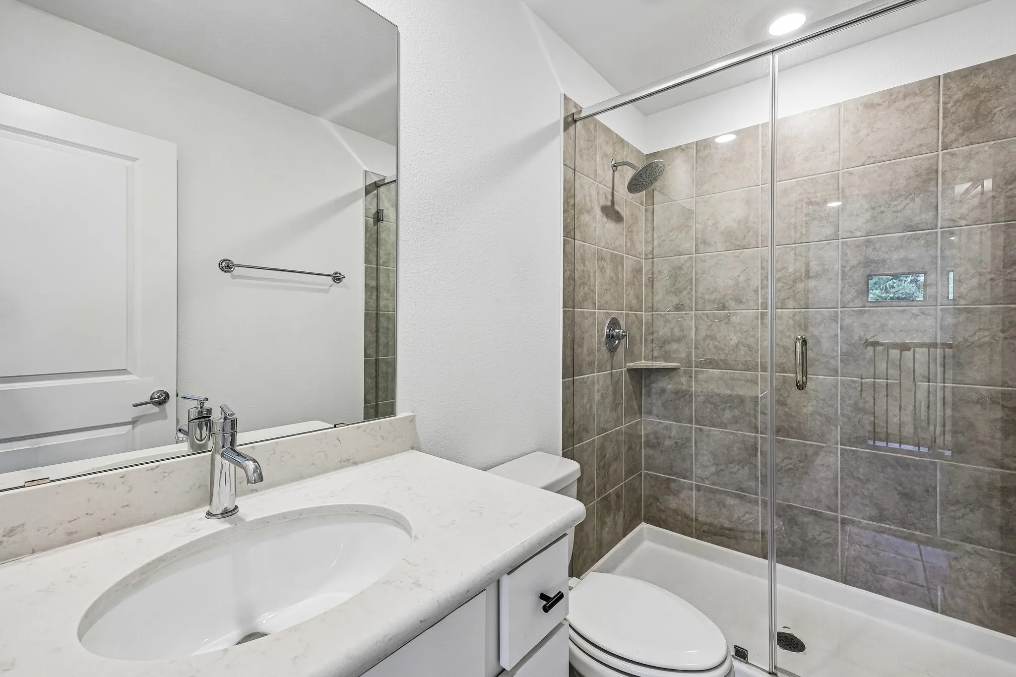 Bathroom featuring a single vanity with an integrated sink and light-toned countertop, chrome faucet, and a frameless mirror
