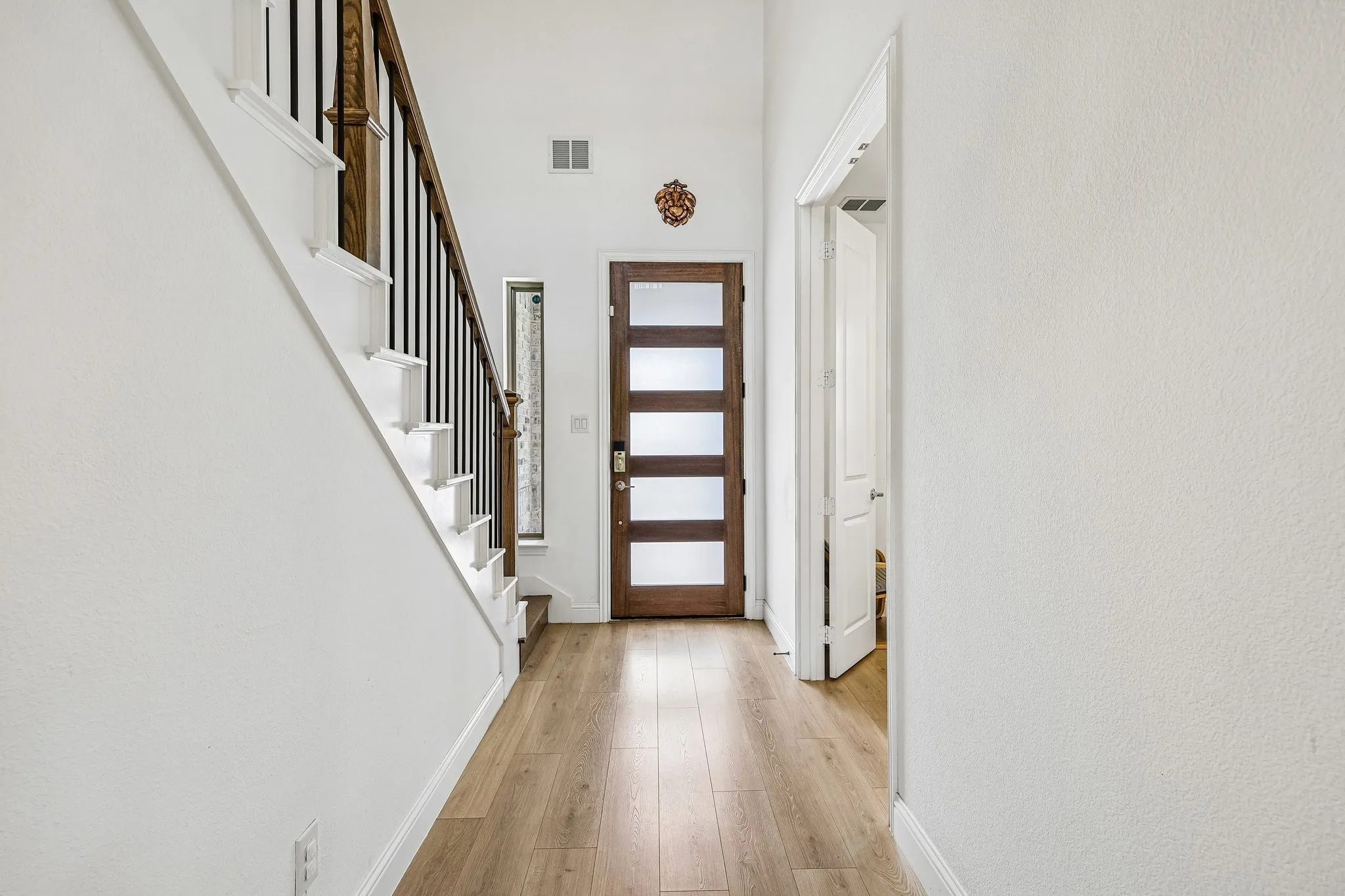 Entryway featuring wood-finish flooring, a contemporary wood-paneled door with frosted glass inserts, and a staircase with white risers and a dark wood handrail with black spindles