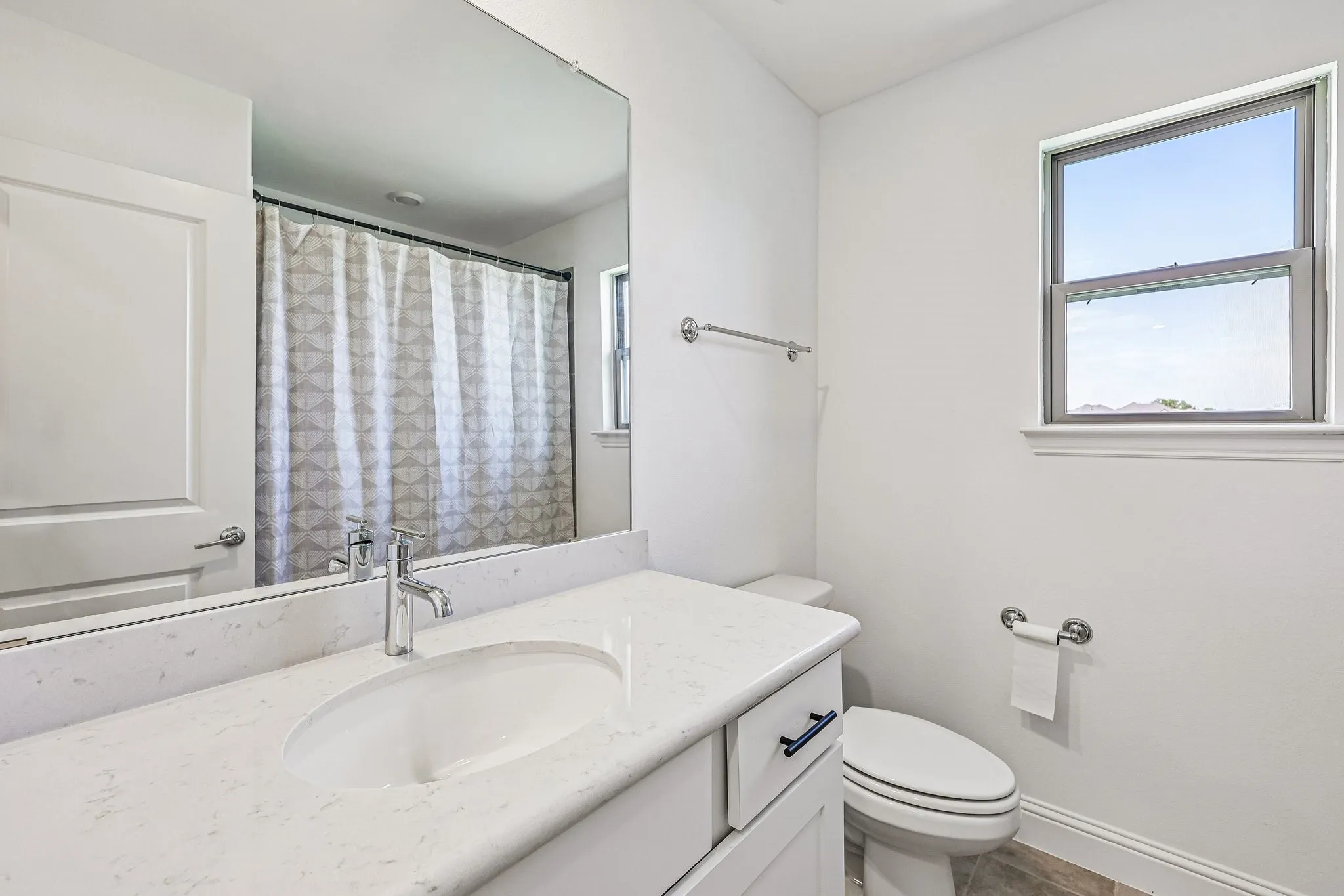 Bathroom featuring a vanity with an undermount sink, a stone-finish countertop, white cabinetry with dark hardware, a large mirror, and a window