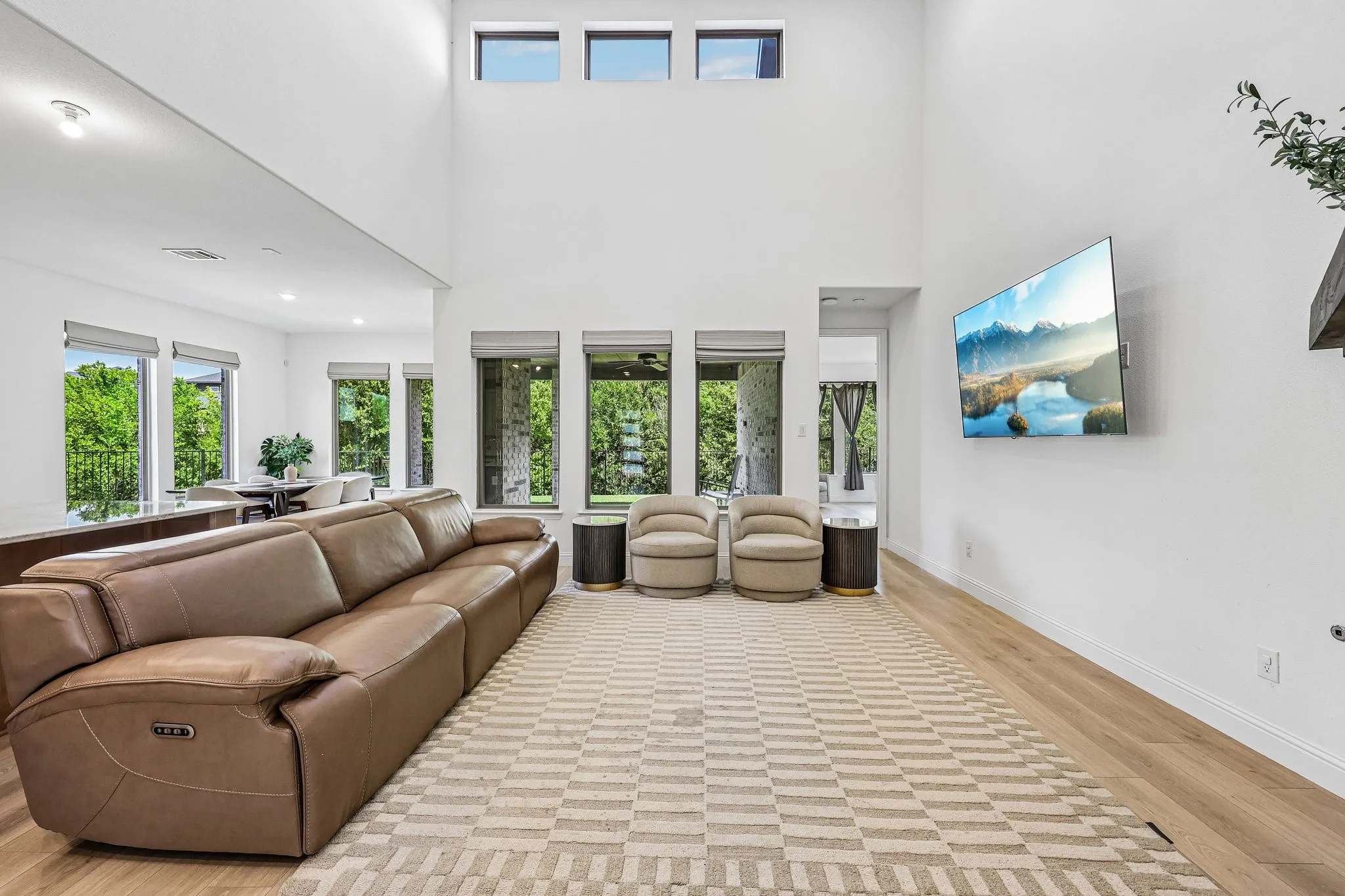 Spacious living area featuring a double-height ceiling, abundant natural light from multiple windows, and wood-finish flooring