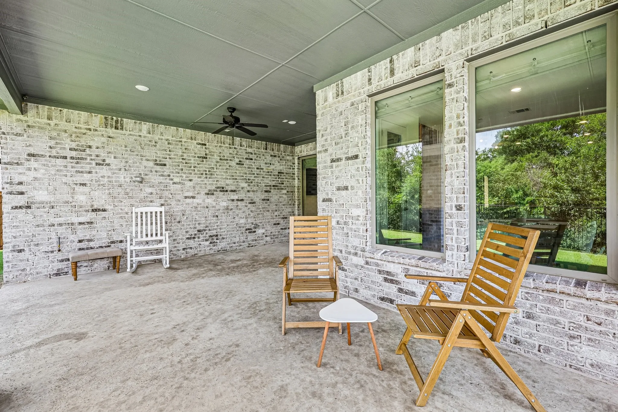 Spacious covered patio with a textured concrete surface, white-washed brick wall, and a ceiling fan