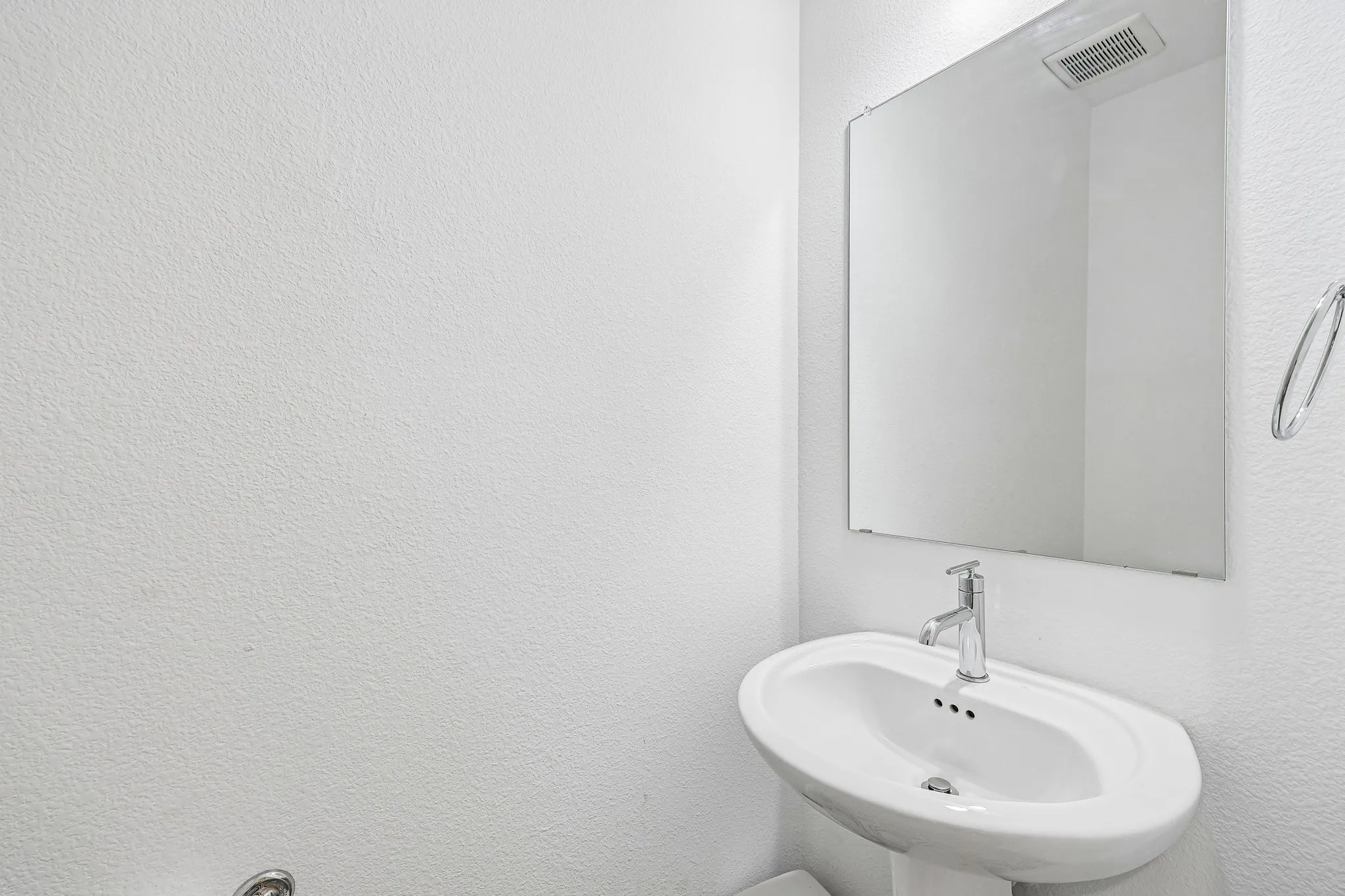 Pedestal sink with chrome faucet, large frameless mirror, and wall-mounted towel ring