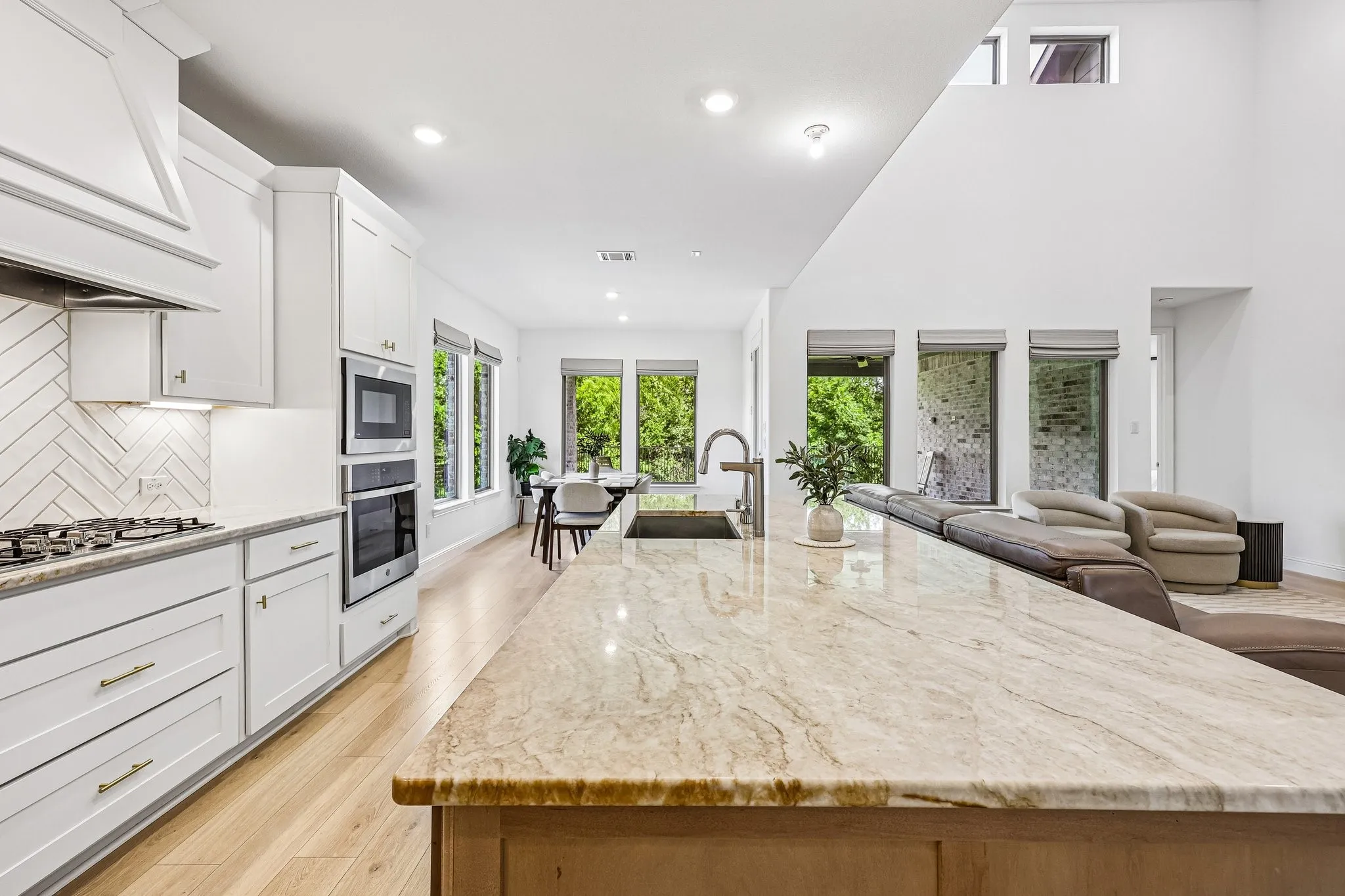 Gourmet kitchen featuring a substantial stone countertop island, white cabinetry, a herringbone tile backsplash, and integrated stainless steel appliances including a built-in double oven and microwave