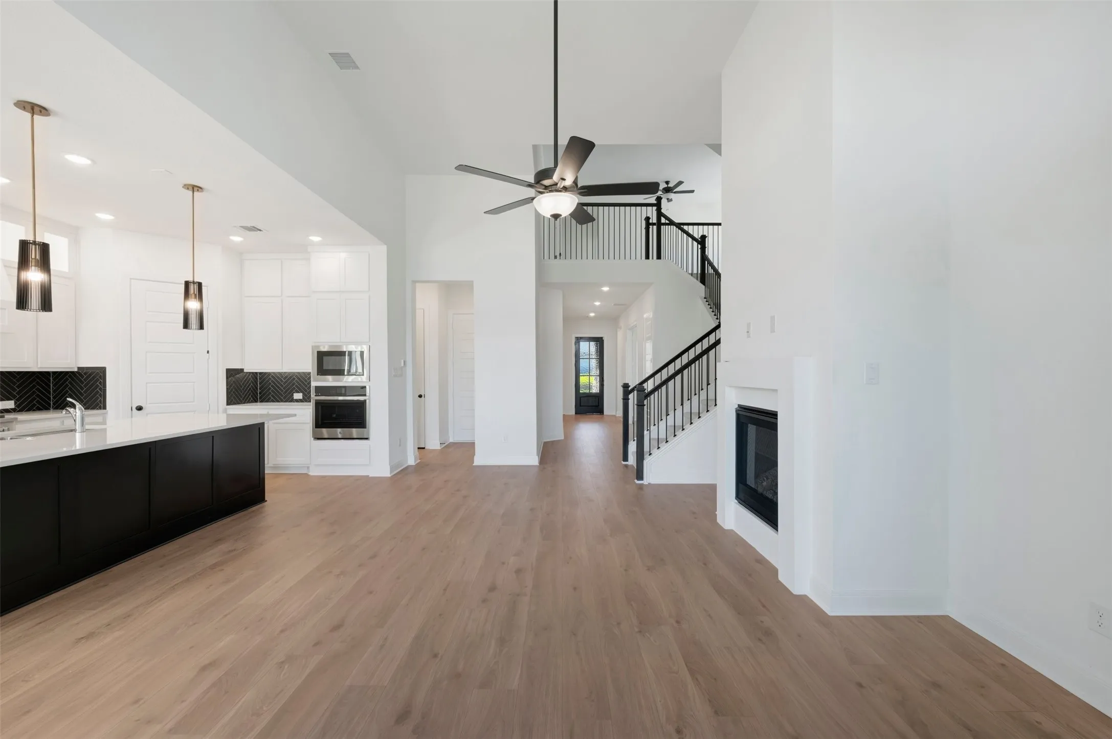 Vaulted ceiling with a ceiling fan, wood-finish flooring, built-in fireplace, and a staircase with black metal balusters