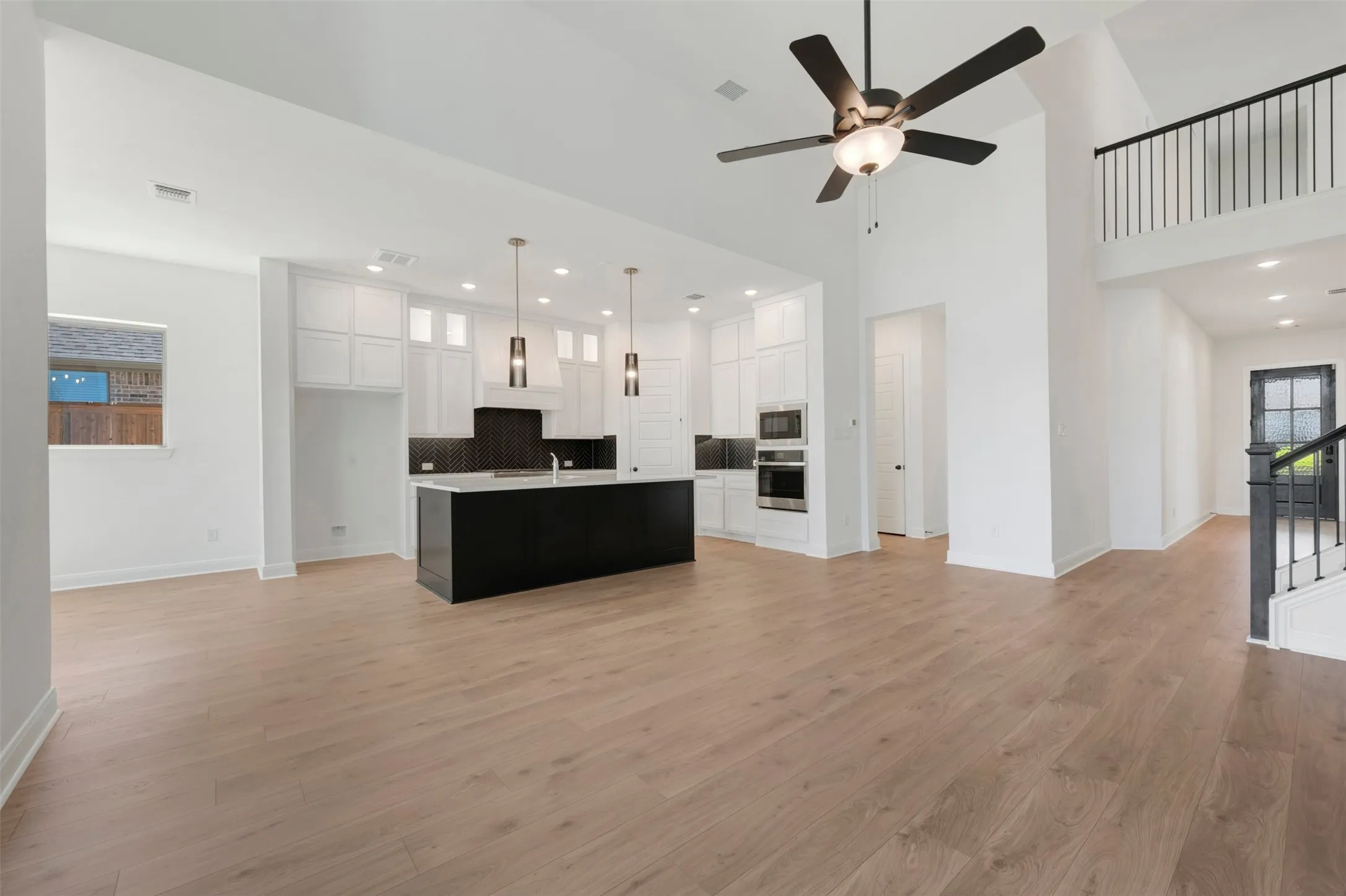 Open-concept living area with wood-finish flooring, a two-story ceiling, and a modern kitchen