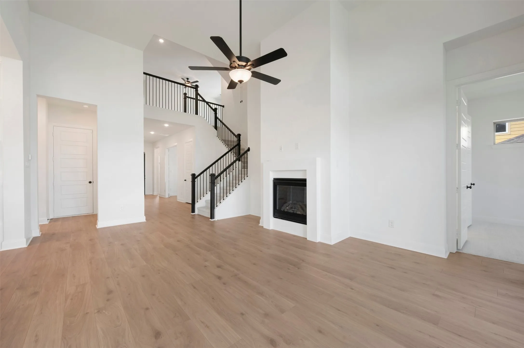 Soaring ceilings with decorative lighting, wood-finish flooring, two-story staircase with dark balusters, and a built-in fireplace