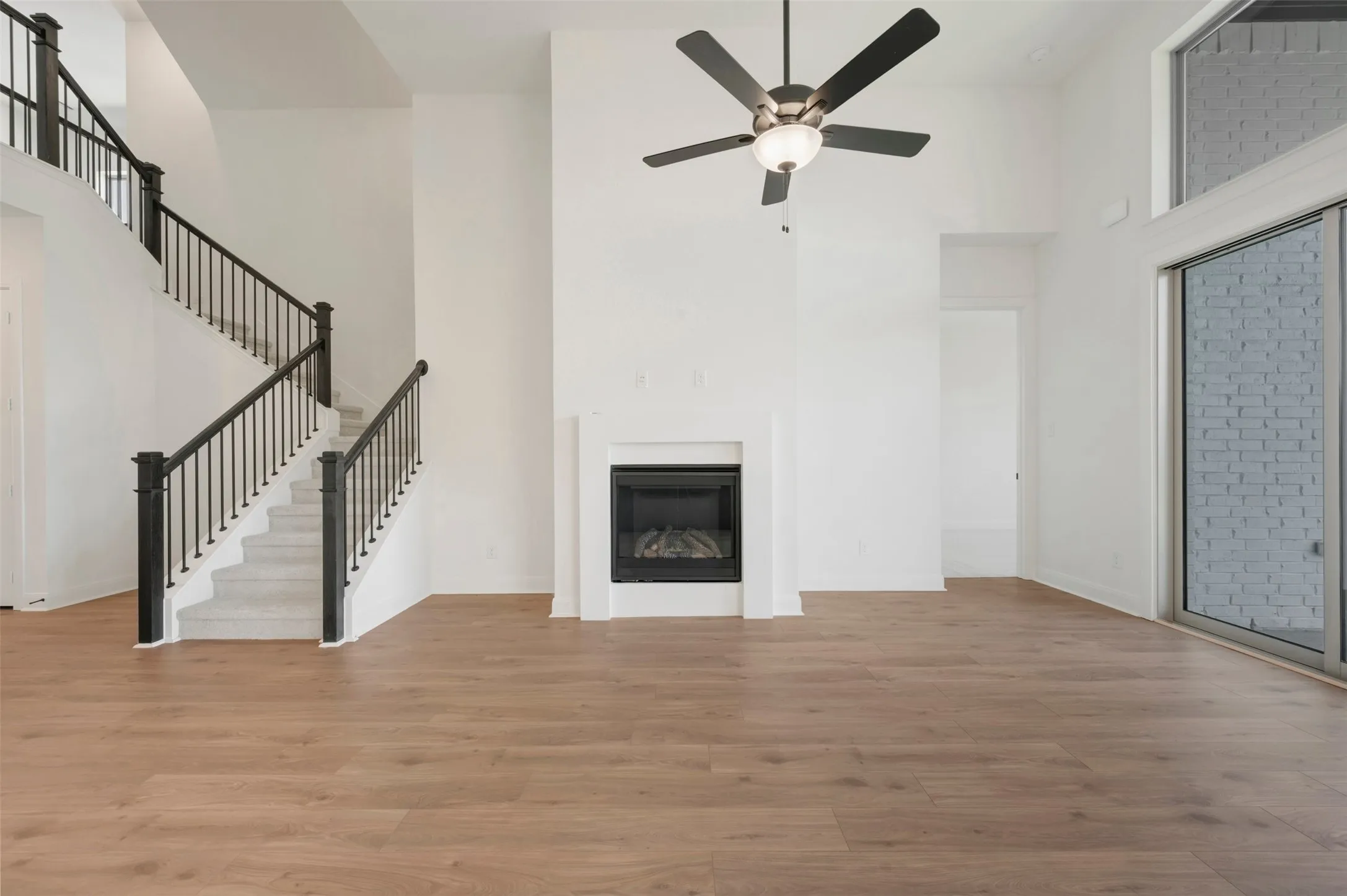 Vaulted ceilings with a ceiling fan, a fireplace with a white surround, wood-finish flooring, a staircase with black railings, and a sliding glass door