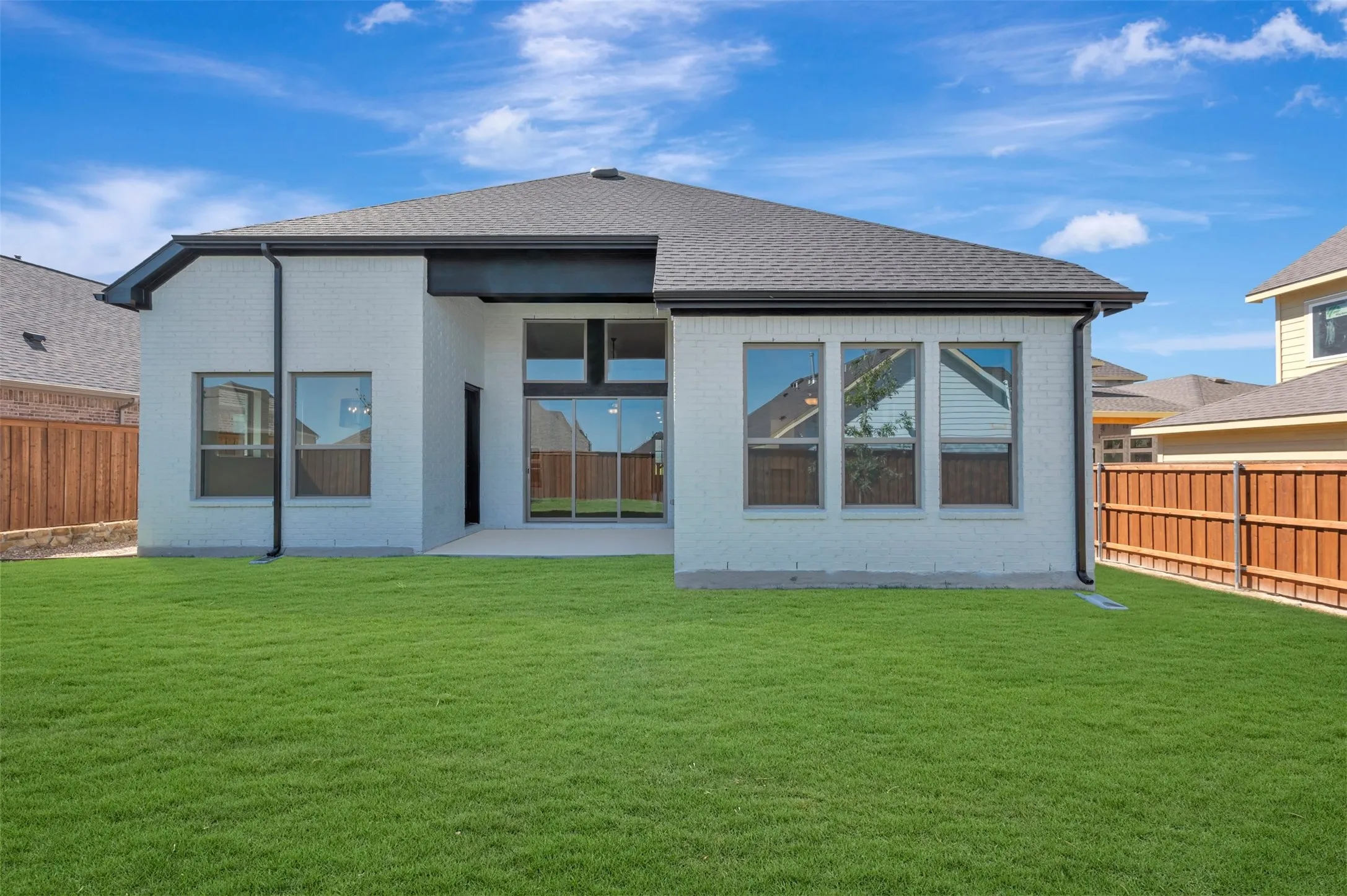 Expansive green lawn, white brick exterior, dark grey roof, patio with sliding glass doors, and privacy fencing
