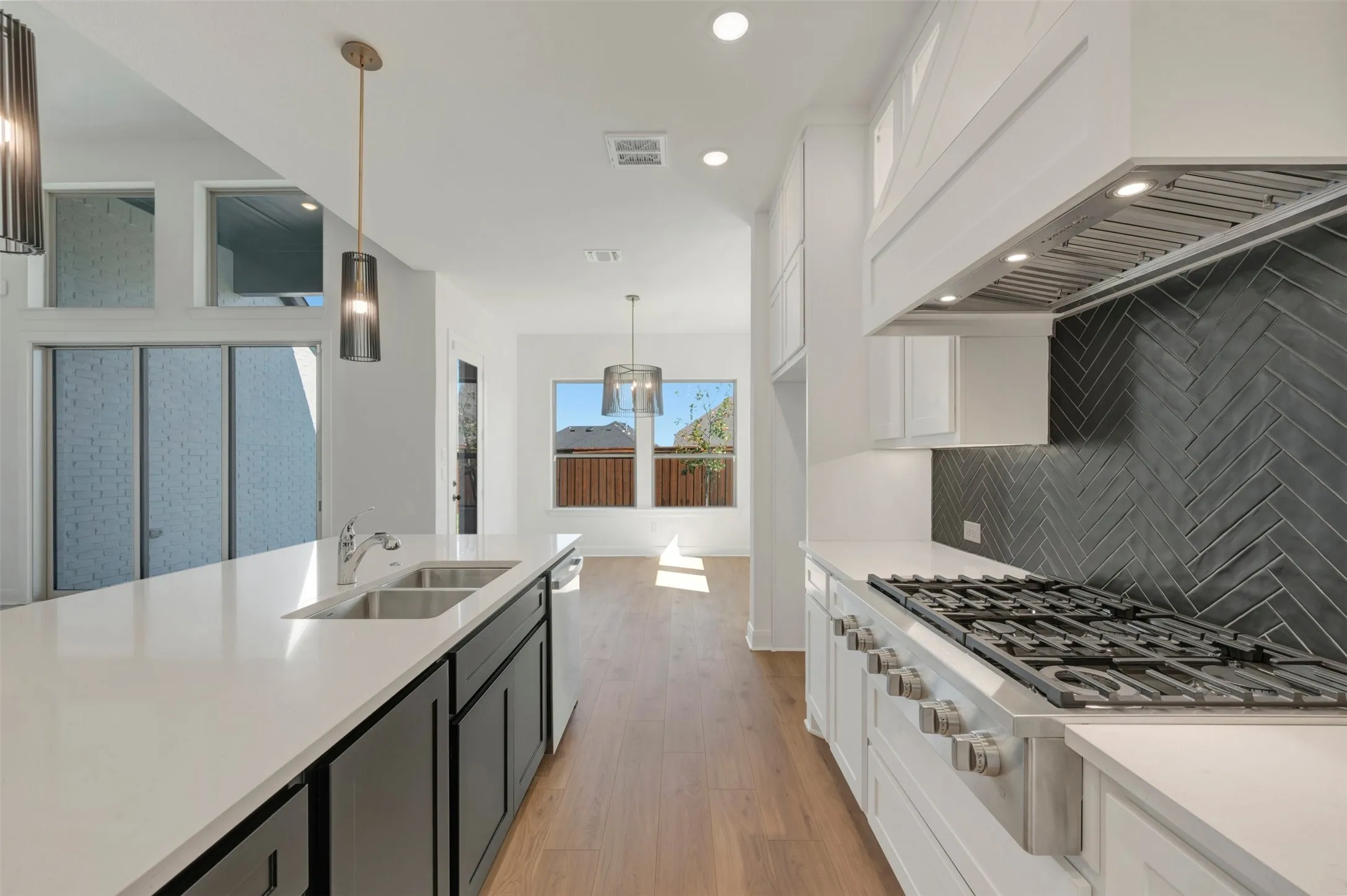 Spacious kitchen featuring an expansive island with an undermount double-basin sink, quartz countertops, a gas range, and a herringbone-patterned tile backsplash